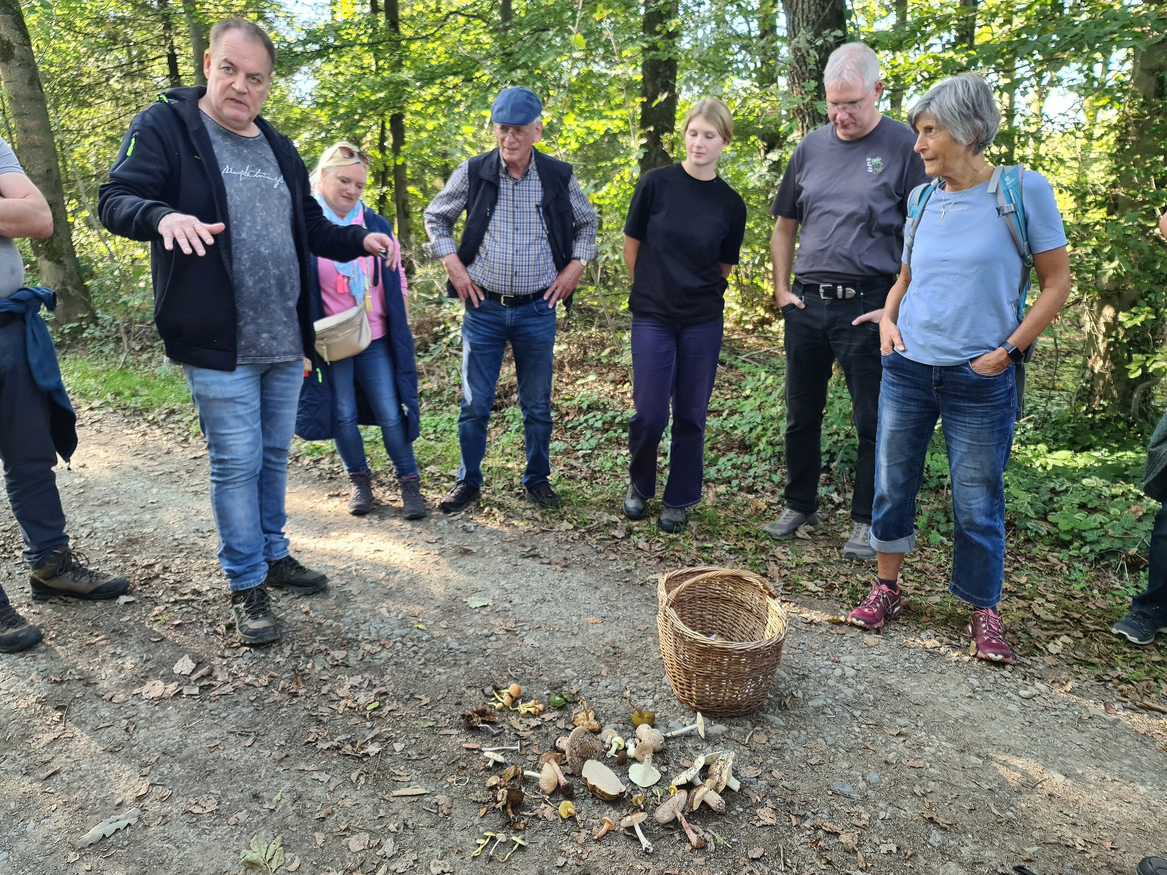Ein Mann spricht im Wald vor einer Gruppe und einem Bastkorb stehend.