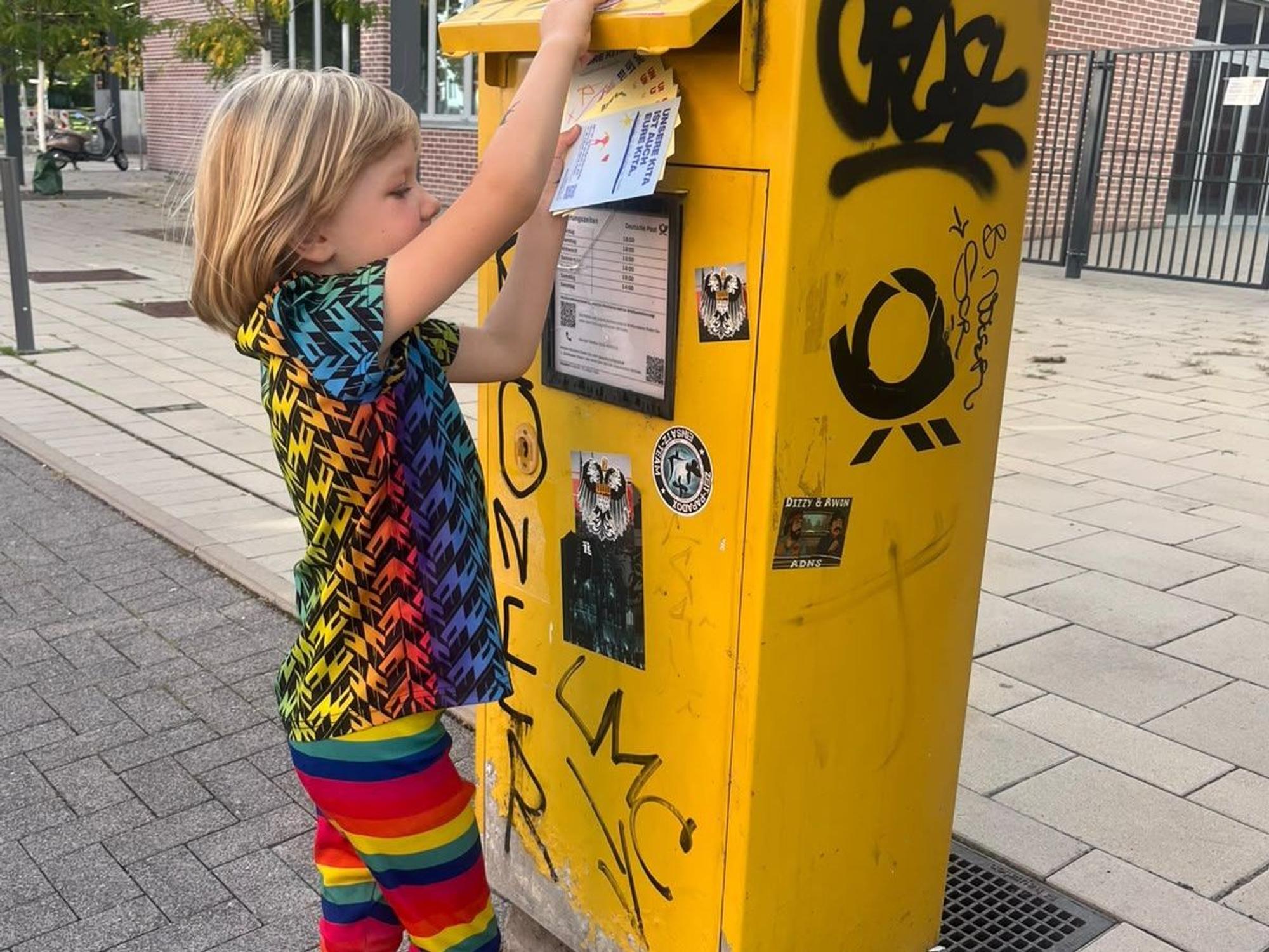 Ein Junge wirft eine Postkarte an ein Mitglied des Jugendhilfeausschusses in den Briefkasten