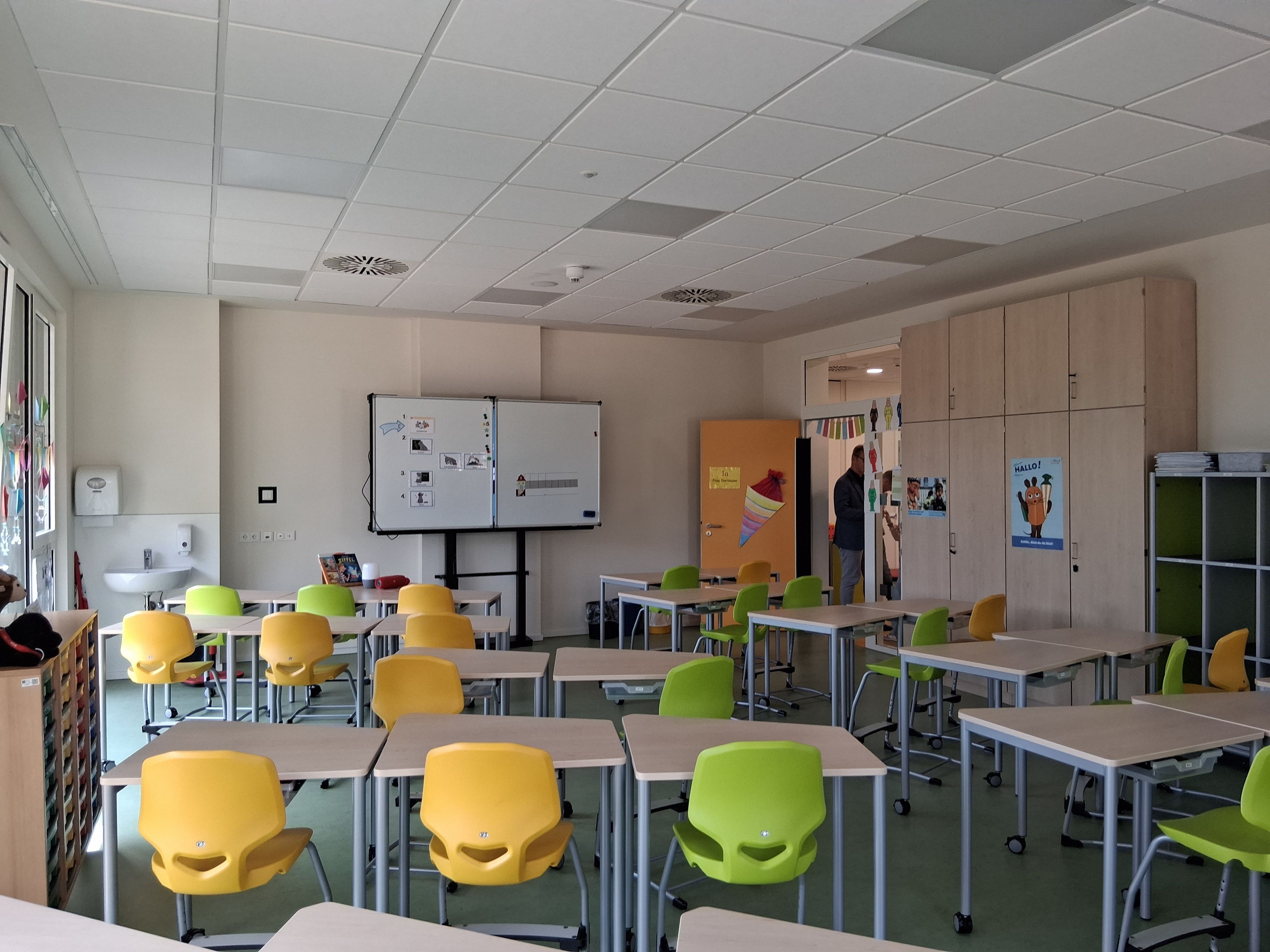 Gelbe und grüne Stühle stehen vor Tischen in einem Klassenraum.