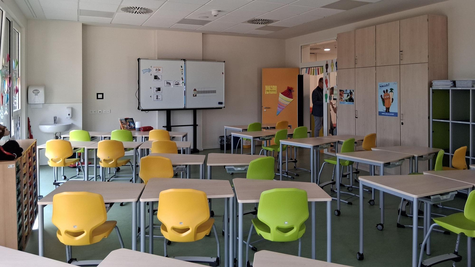 Gelbe und grüne Stühle stehen vor Tischen in einem Klassenraum.