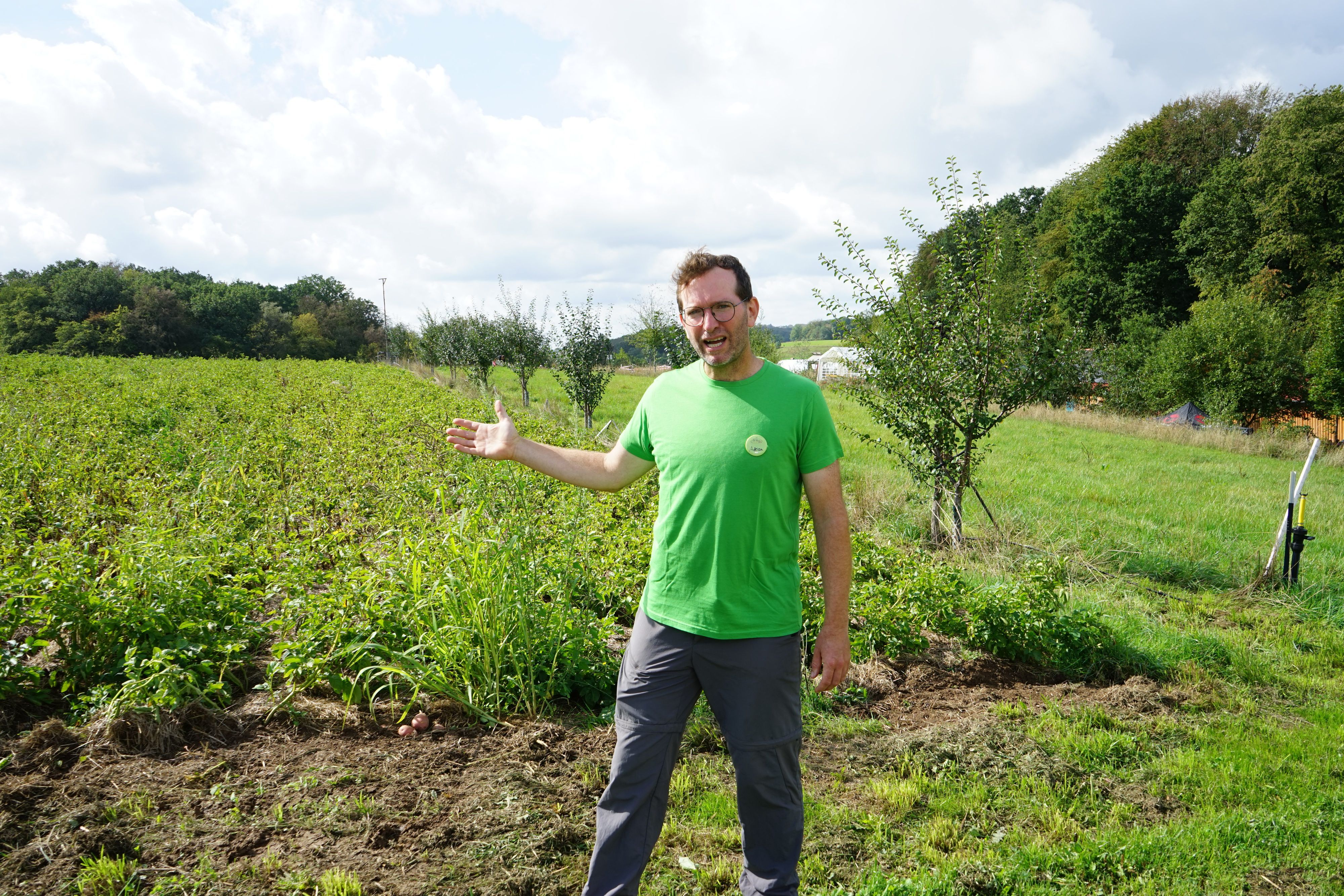 Ein Mann zeigt auf die Felder des Hofes.