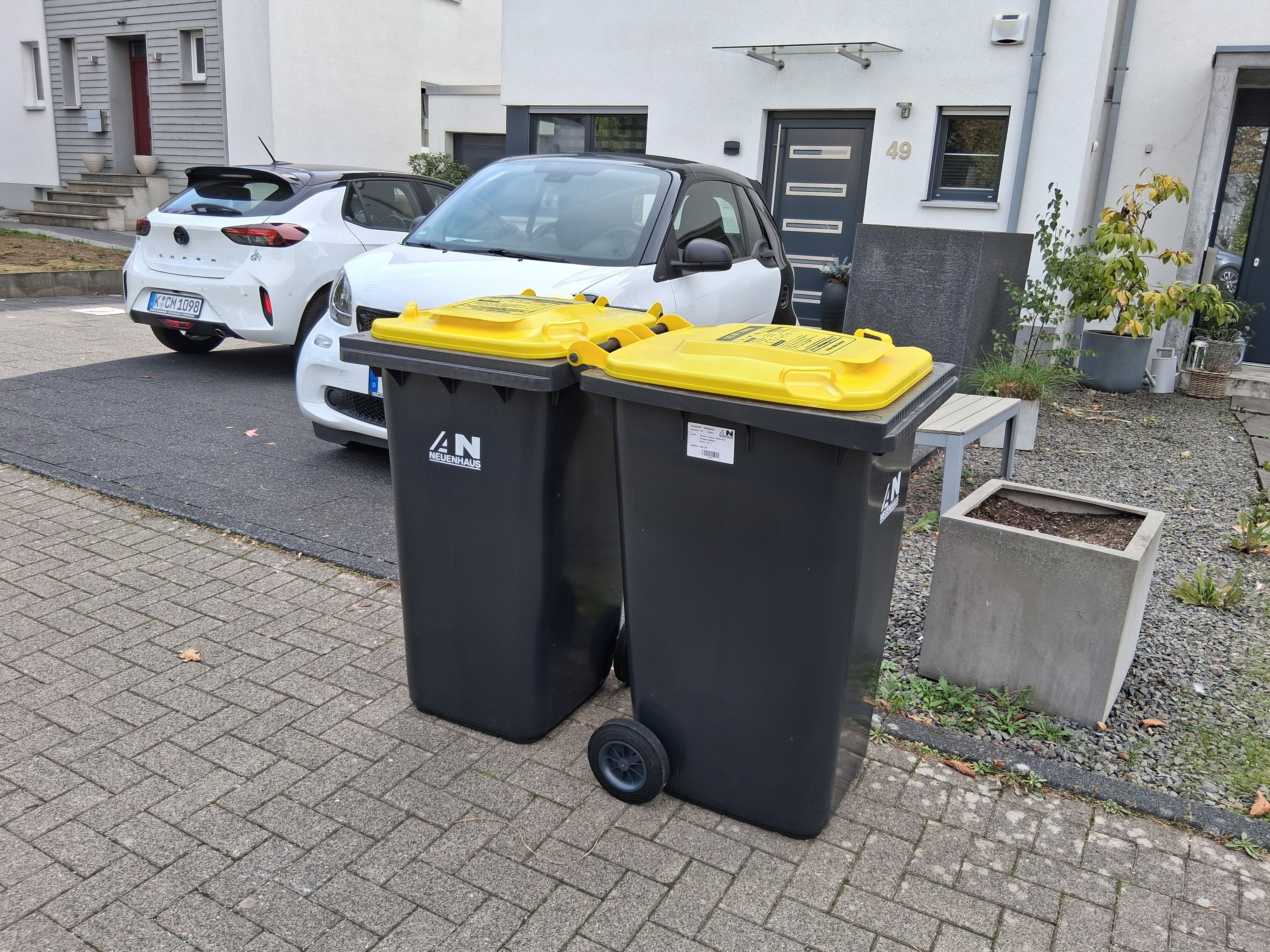 Zwei Gelbe Tonnen stehen auf dem Bürgersteig vor einem Haus.