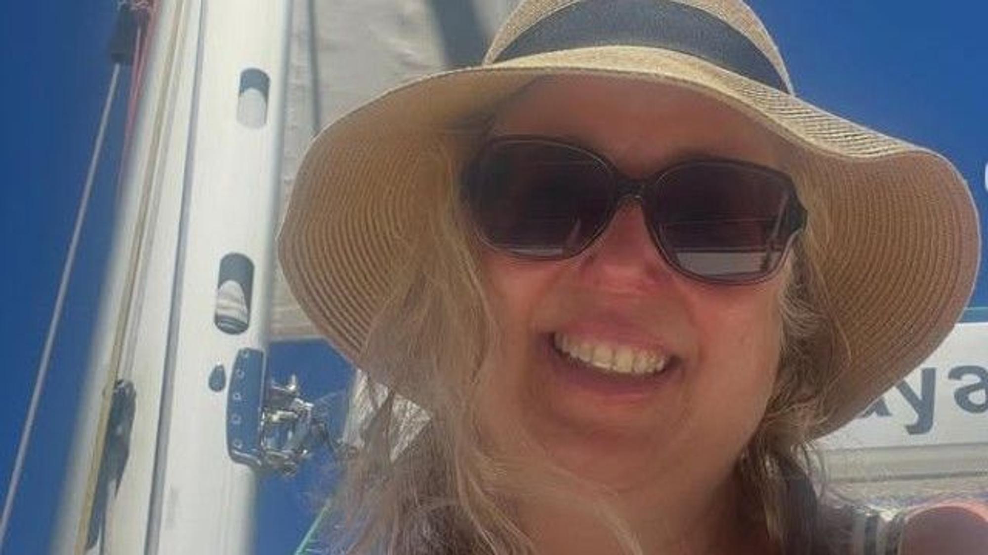 Eine Frau mit Strohhut und Sonnenbrille lacht in die Kamera
