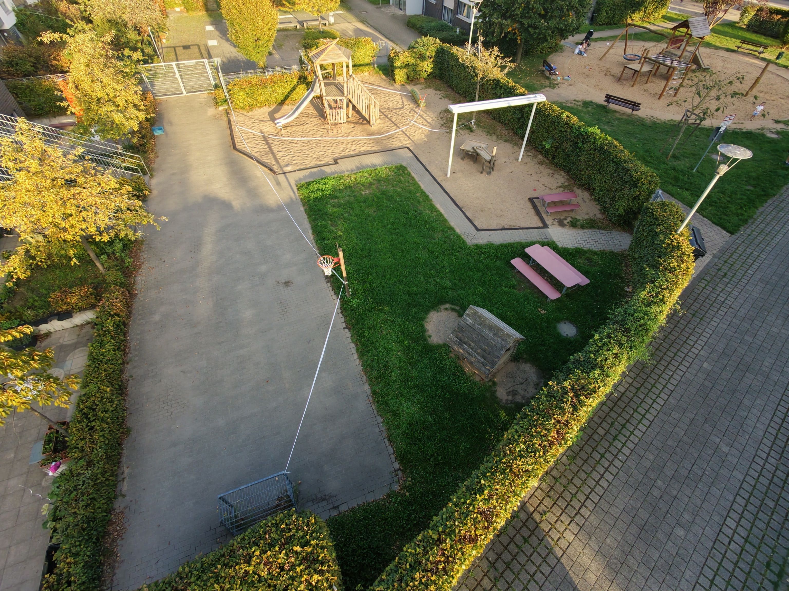 Ein Spielplatz mit Klettergerüst, Sandflächen und Sitzbänken ist aus der Vogelperspektive zu sehen; Absperrband verläuft um den Bereich.