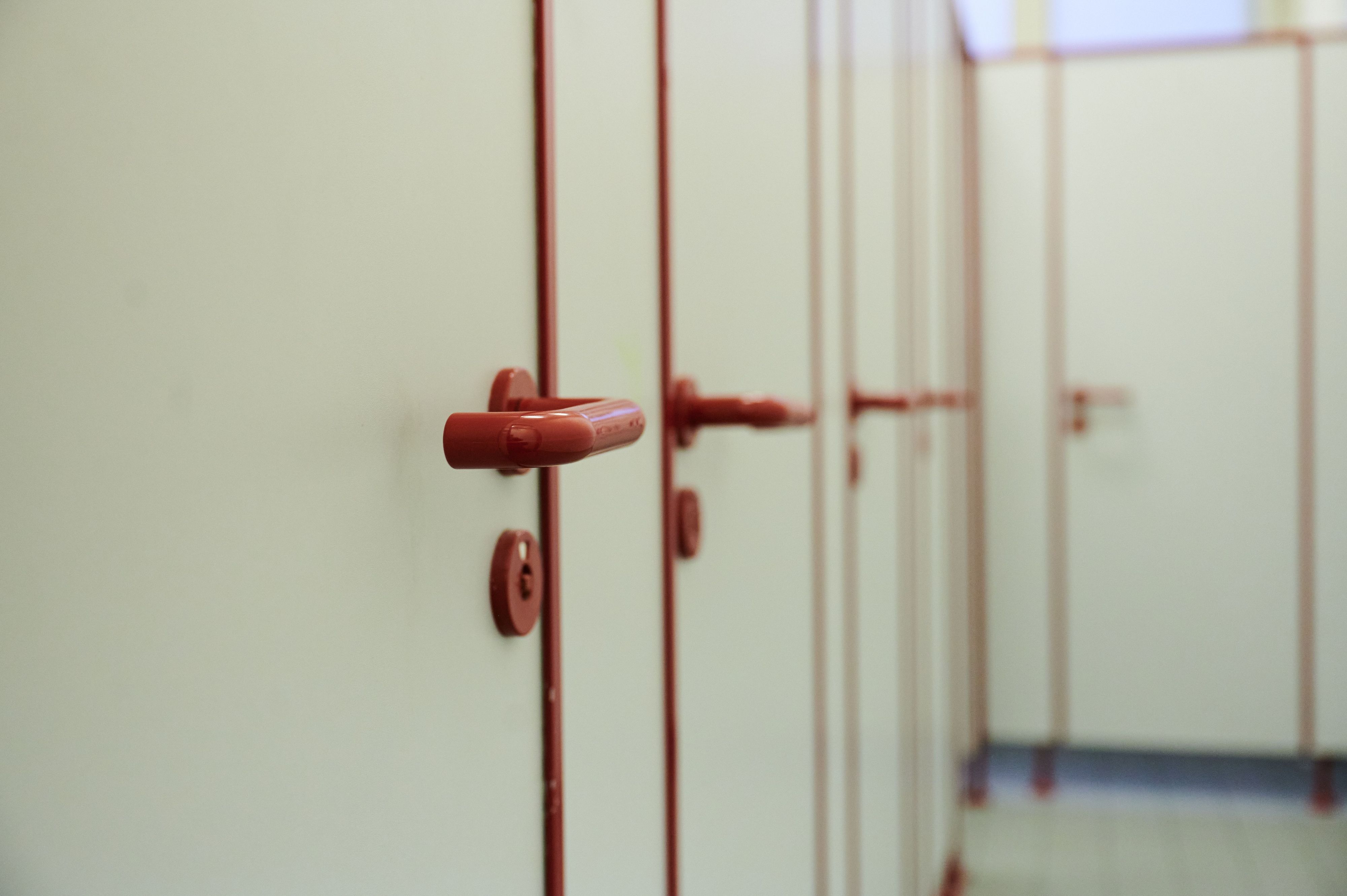 Die Türen mit roten griffen von Toiletten in einer Schule sind zu sehen.