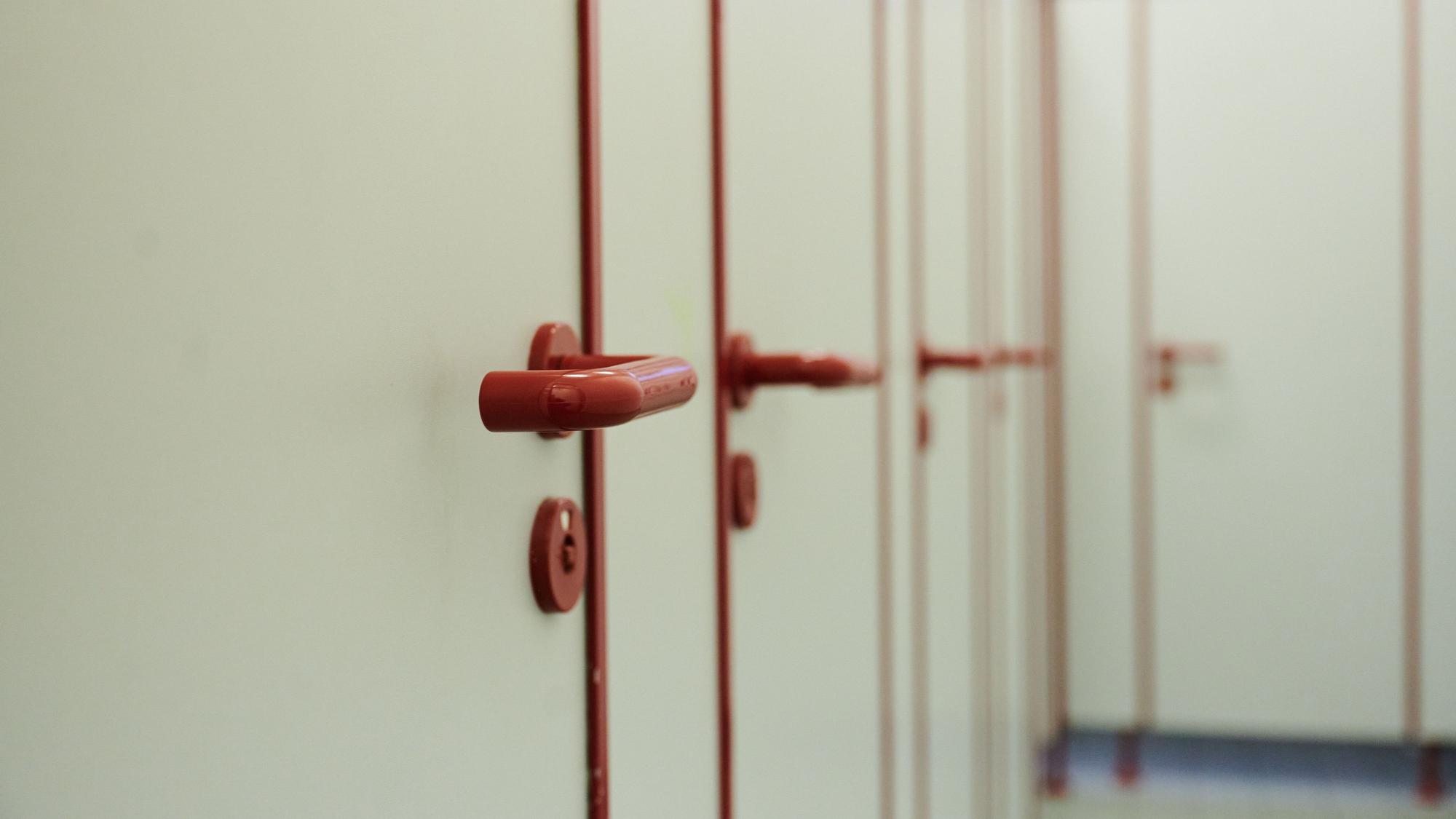 Die Türen mit roten griffen von Toiletten in einer Schule sind zu sehen.