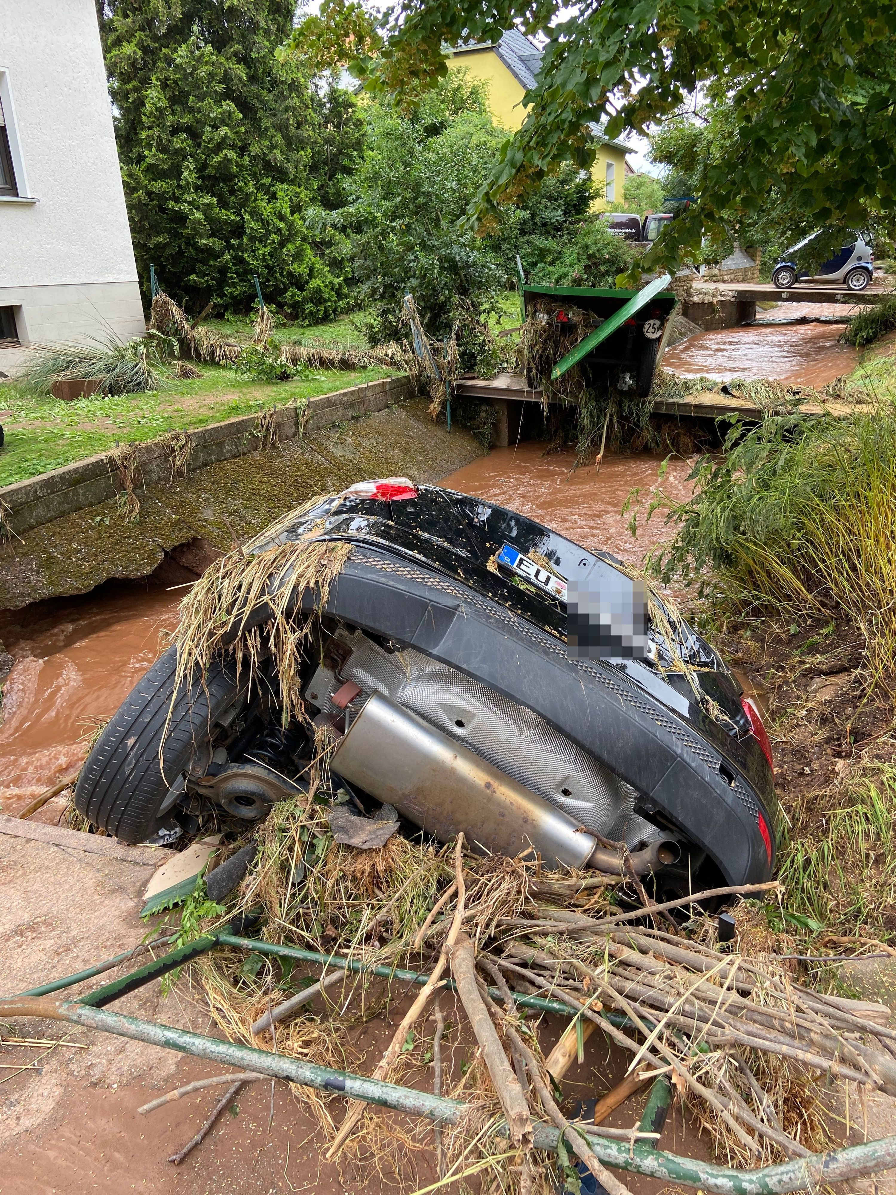 Ein schwarzes Auto hängt an einer Brücke in den Bach.