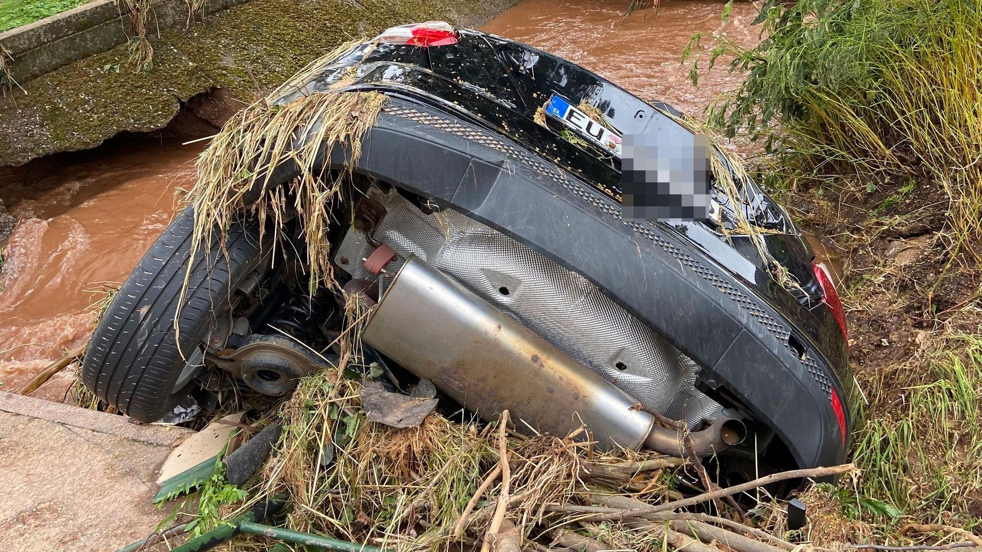 Ein schwarzes Auto hängt an einer Brücke in den Bach.