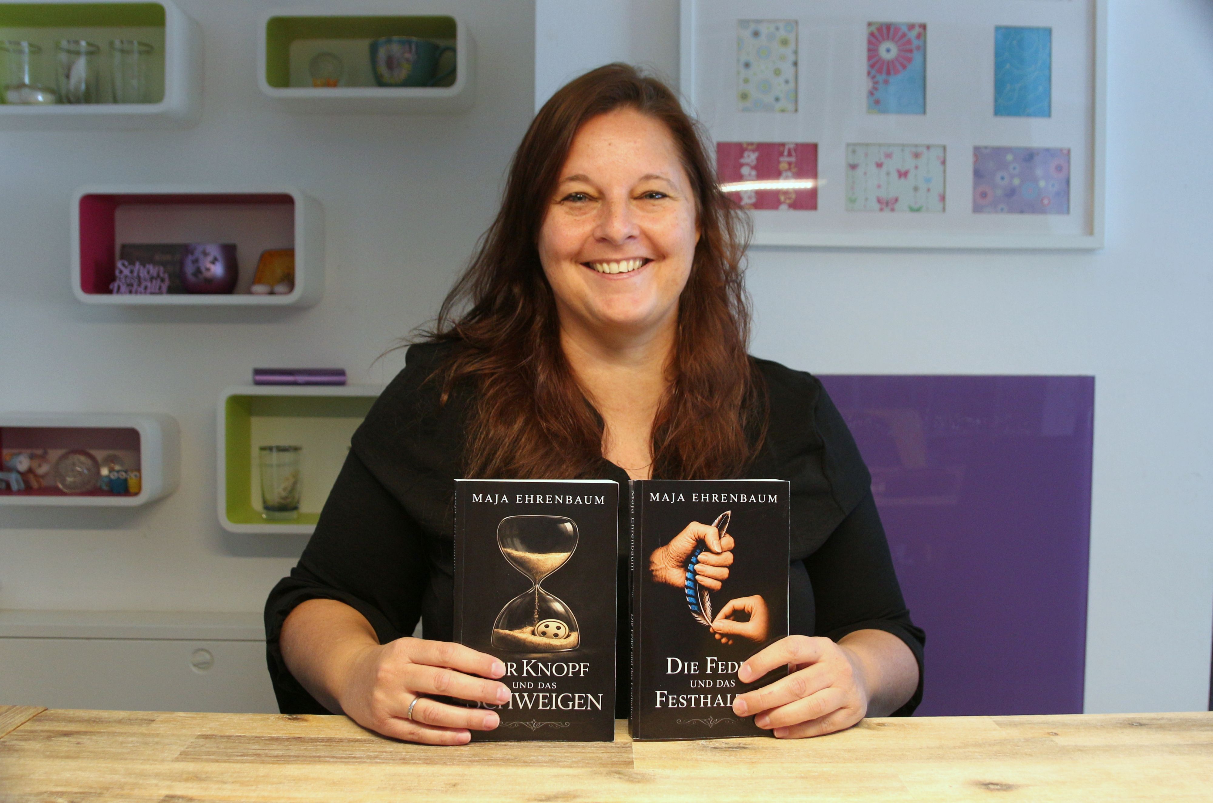 Eine Frau lächelt in die Kamera, sie hält zwei Bücher in ihren Händen.