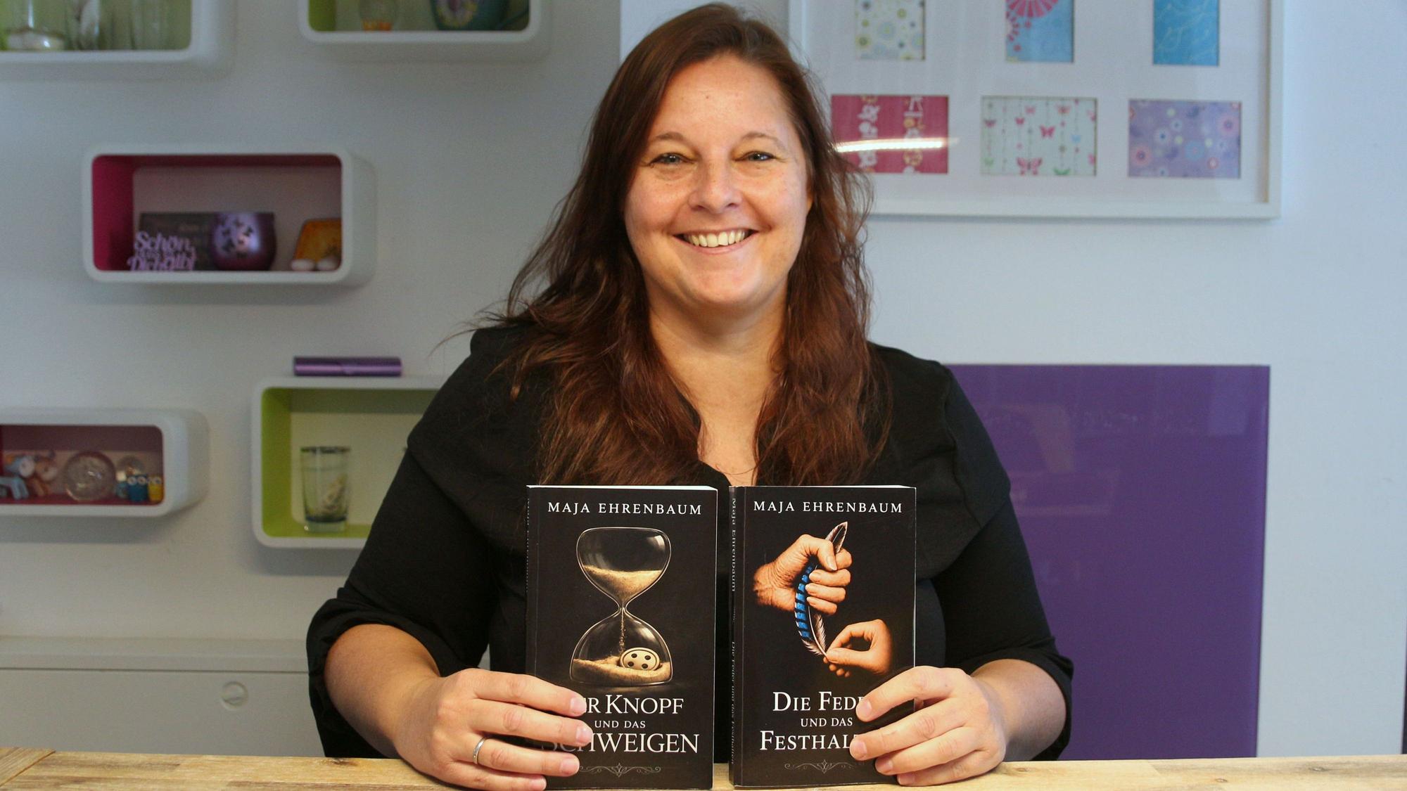Eine Frau lächelt in die Kamera, sie hält zwei Bücher in ihren Händen.
