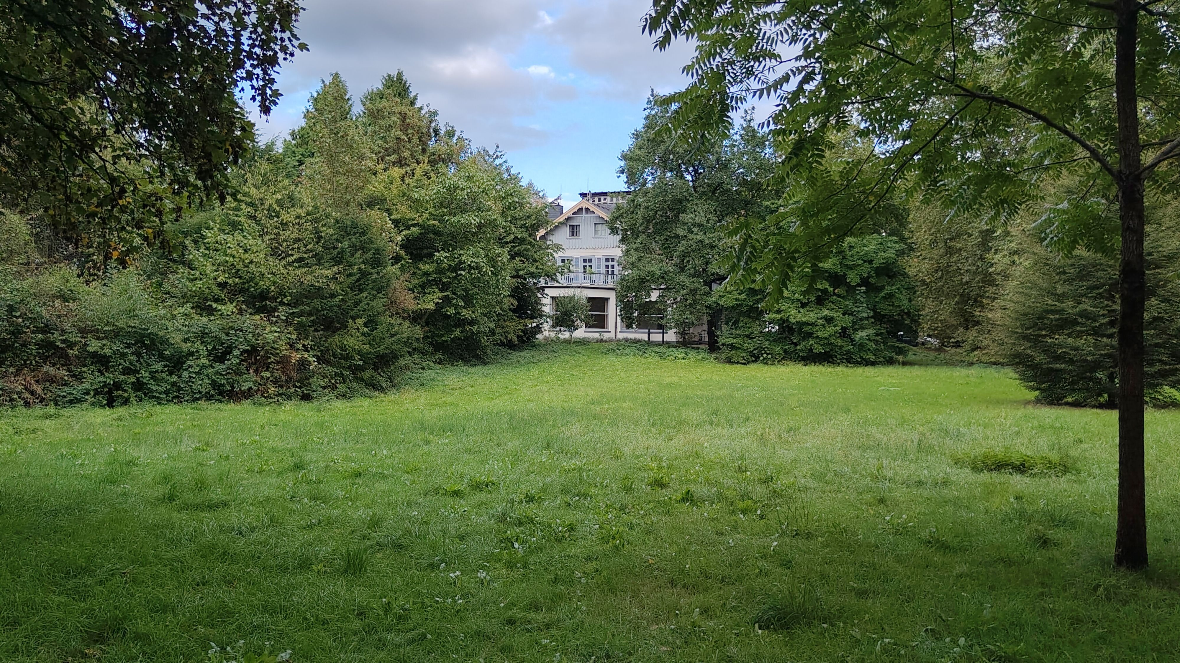Es ist eine große Wiese und die Villa Wuppermann von hinten zu sehen.
