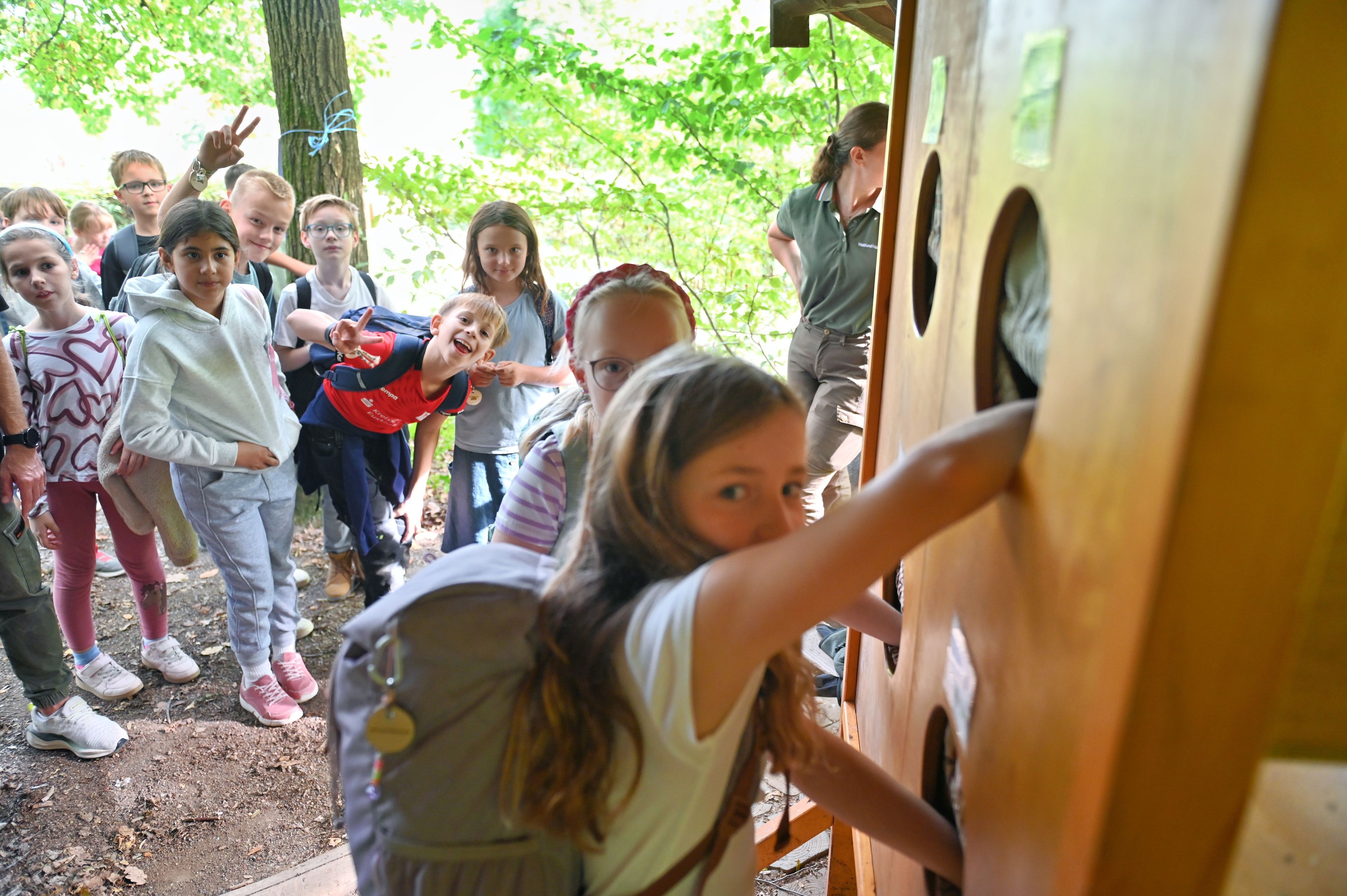 Ein Mädchen greift in ein kreisrundes Loch einer Holzwand, andere Kinder schauen zu.