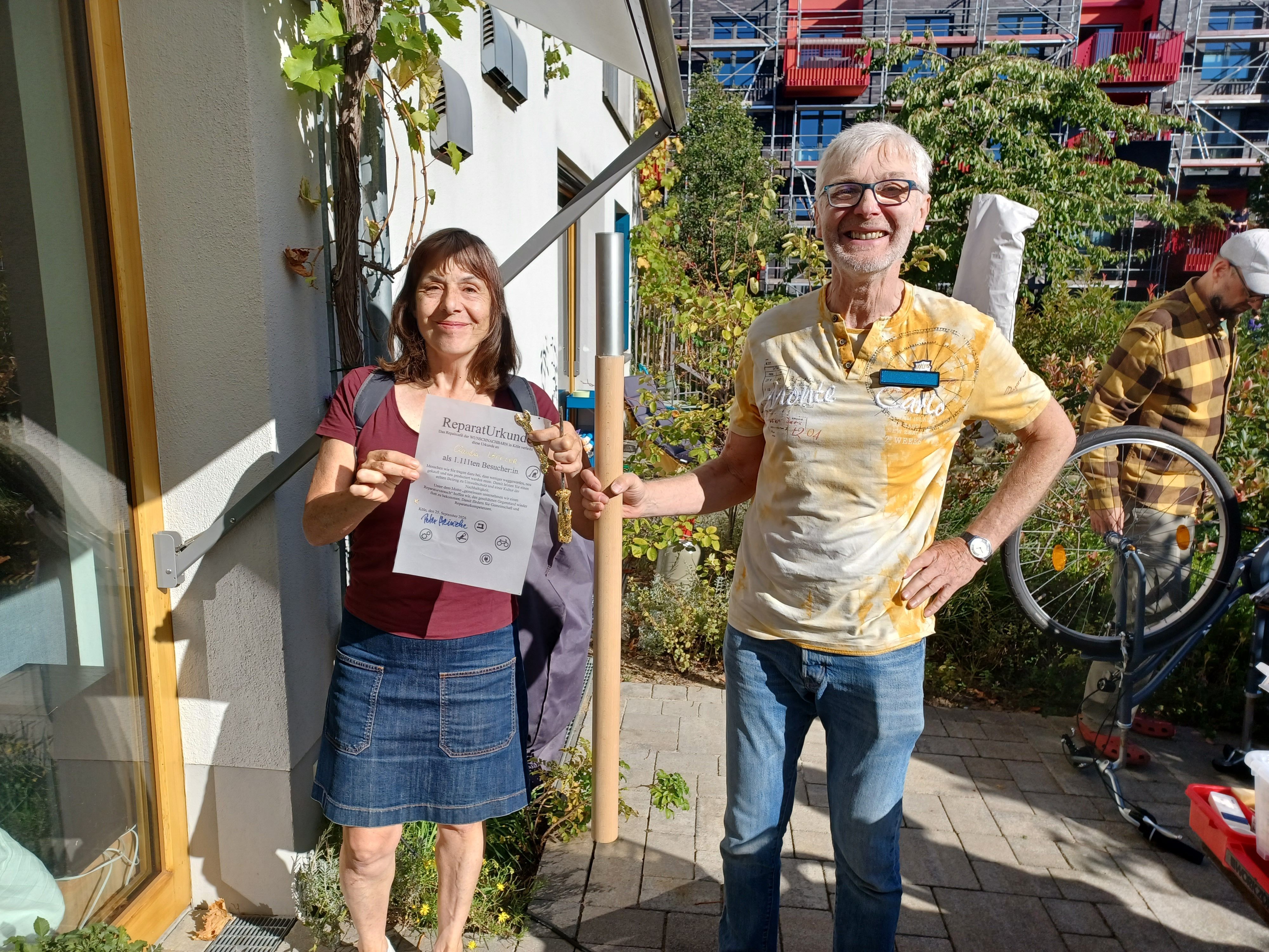 Eine Frau im Minirock steht neben einem Mann im gelben T-Shirt und Jeans. Er hält einen Holzstab in der Hand.