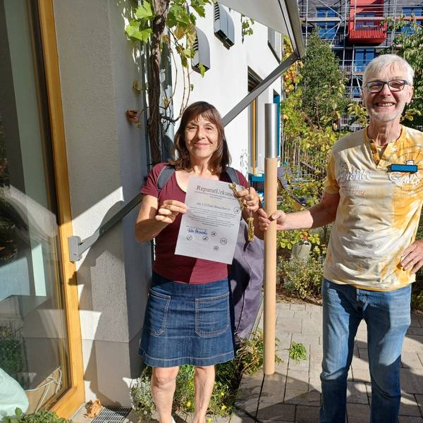 Eine Frau im Minirock steht neben einem Mann im gelben T-Shirt und Jeans. Er hält einen Holzstab in der Hand.