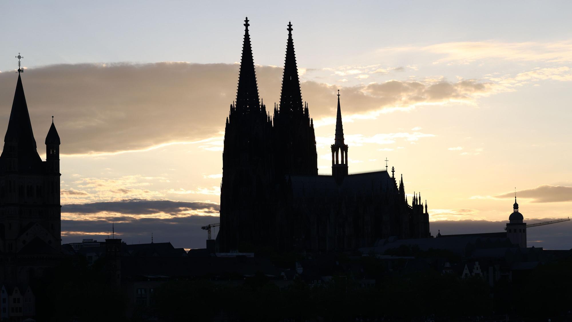 Der Kölner Dom zeichnet sich als Silhouette vor der untergehenden Sonne ab.