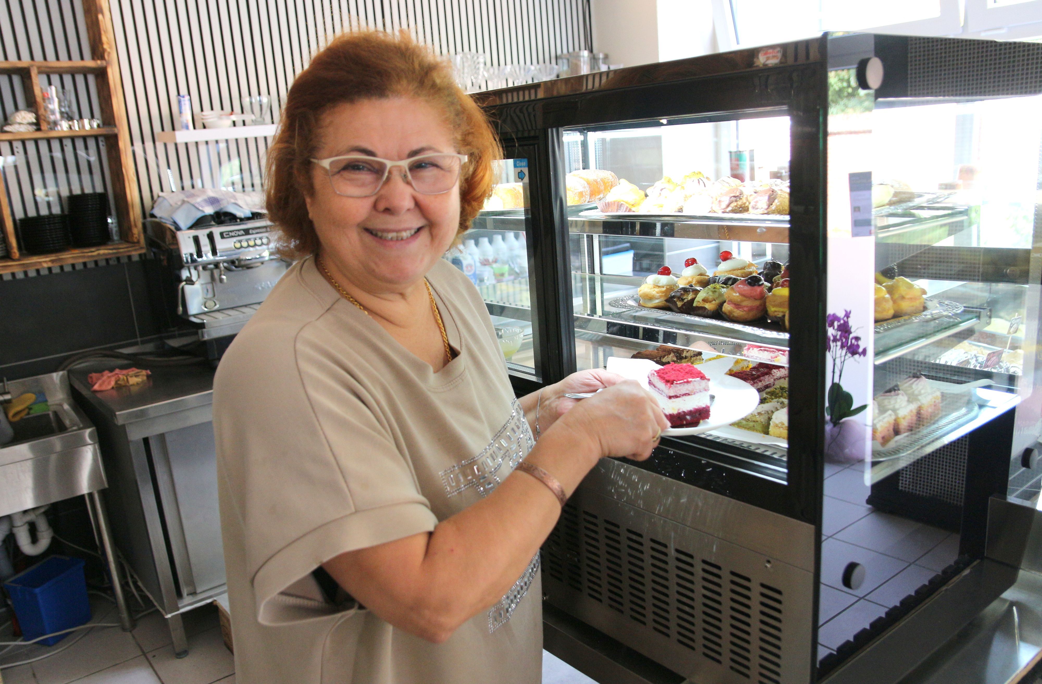 Eine Frau lächelt in die Kamera, in der Hand hält sie einen Teller mit einem Stück Kuchen.
