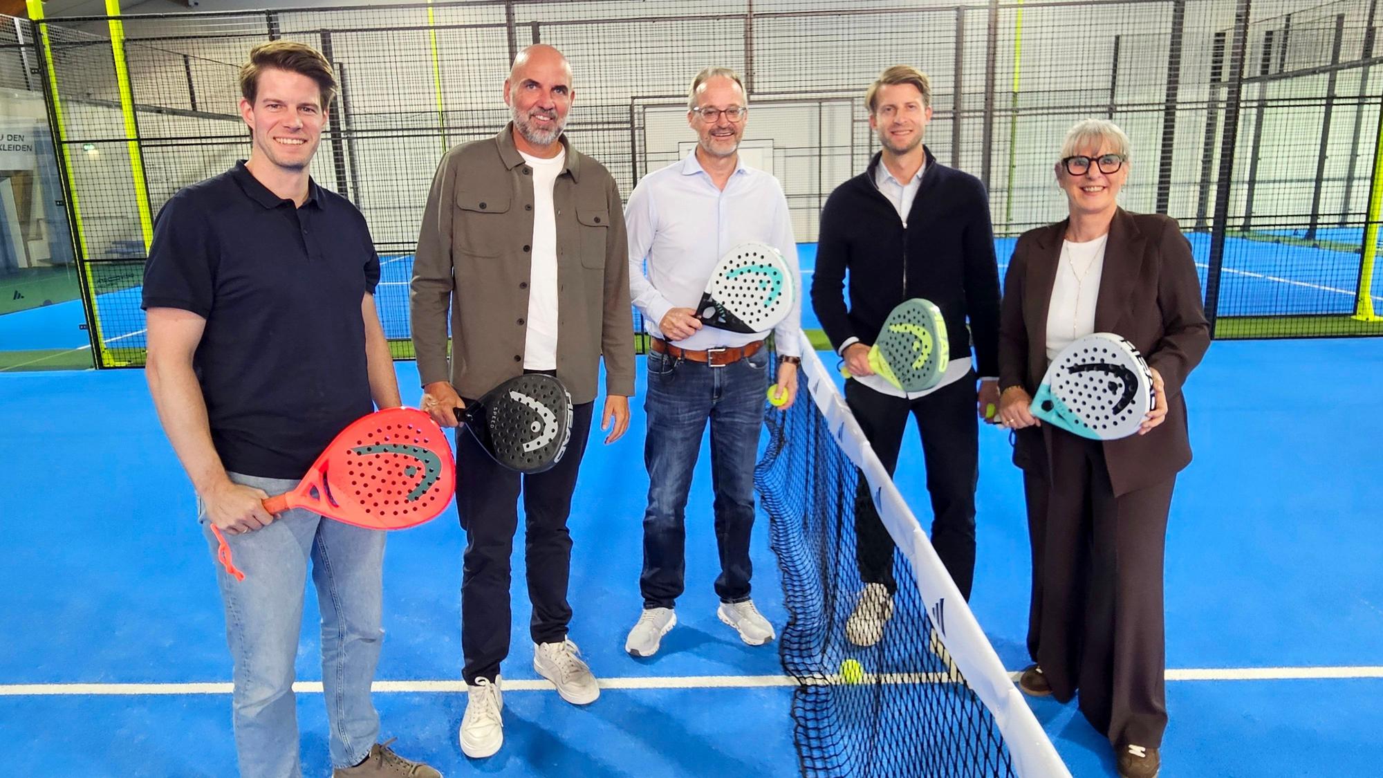 Vier Männer und eine Frau mit Padel-Schlägern stehen am Netz.