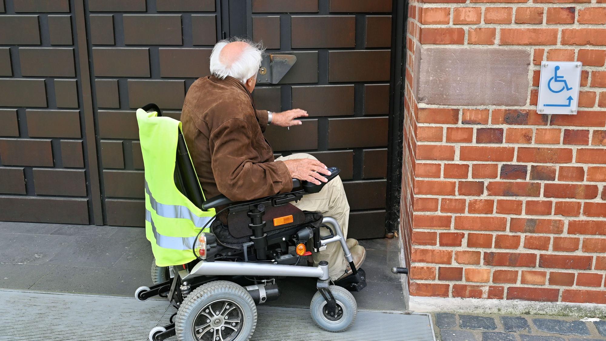 Ein älterer Mann, der in einem E-Rollstuhl sitzt, an der Eingangstür zur Pfarrkirche St. Peter in Zülpich.