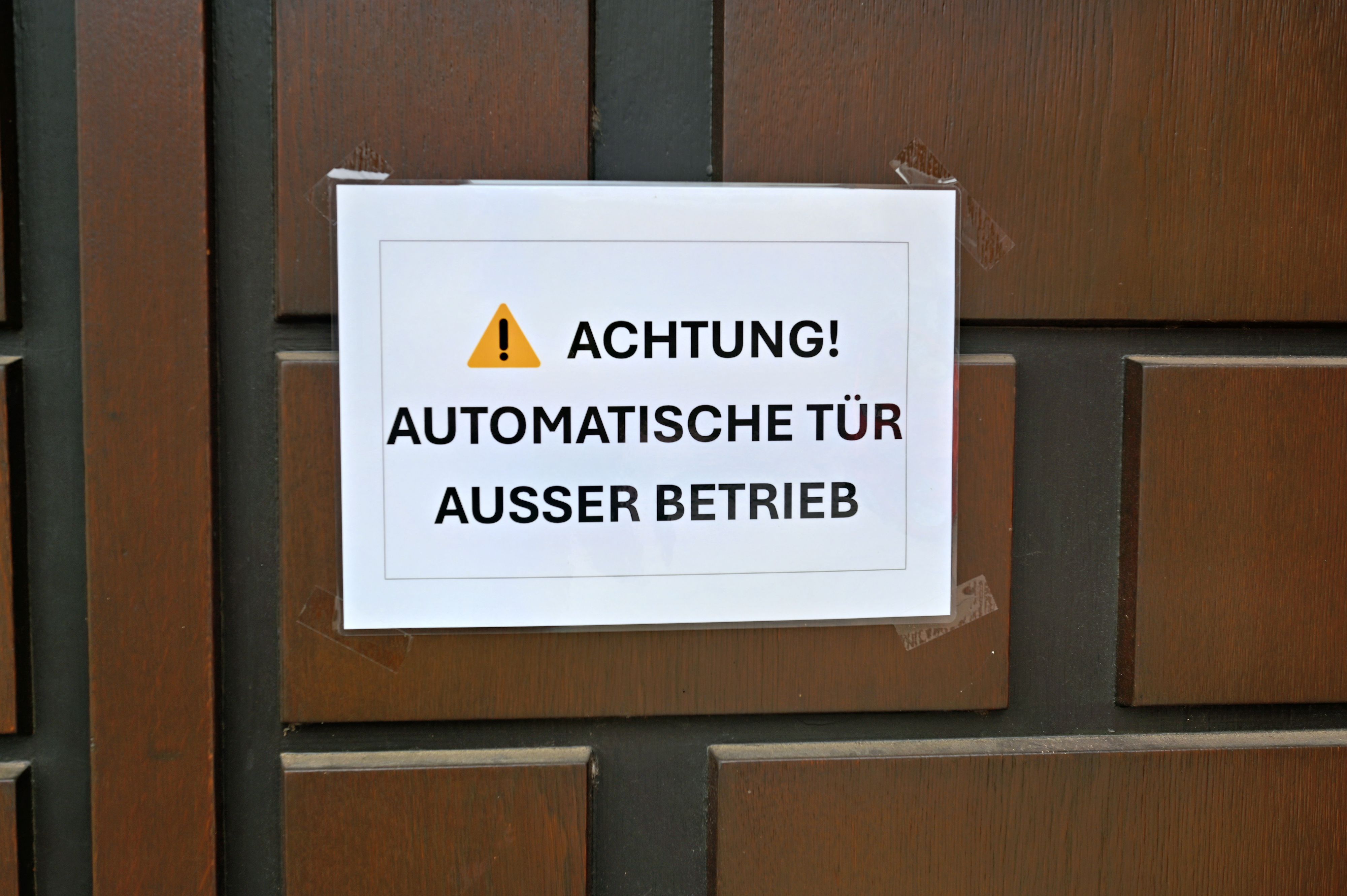 Ein kleines Hinweisschild weist auf den Deffekt der automatischen Eingangstür der Pfarrkirche St. Peter in Zülpich hin.