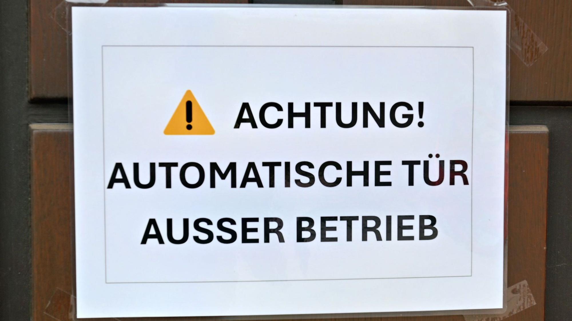Ein kleines Hinweisschild weist auf den Deffekt der automatischen Eingangstür der Pfarrkirche St. Peter in Zülpich hin.