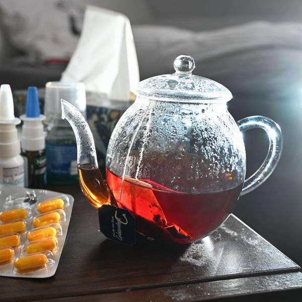 Medikamente und eine Kanne und Tasse Tee zur Bekämpfung einer Erkältung sind auf einem Nachttisch aufgestellt.