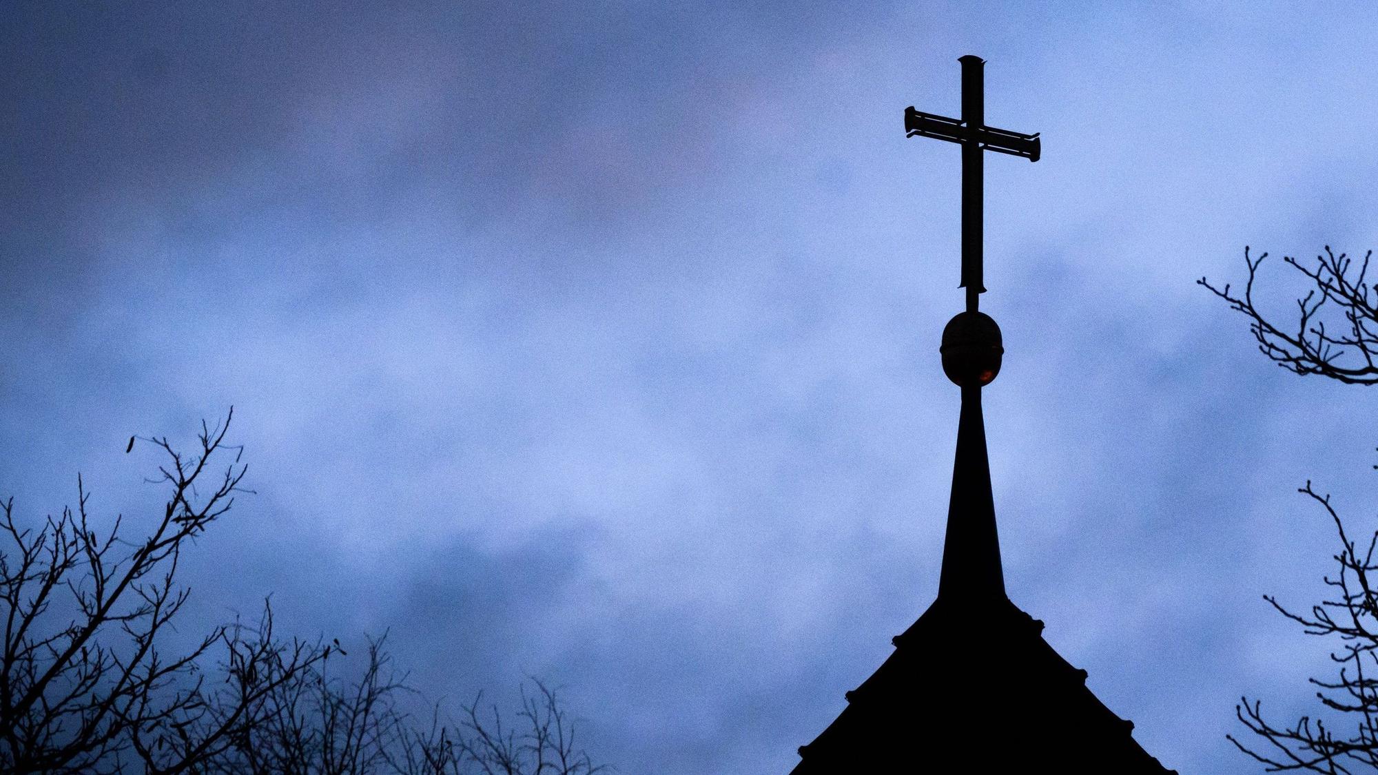 ARCHIV - 25.01.2024, Niedersachsen, Hannover: Dunkle Wolken ziehen über das Kreuz auf einer evangelischen Kirche in der Region Hannover hinwe (zu dpa: «Studie in zwei Bistümern: Machtmissbrauch in Gemeinschaften») Foto: Julian Stratenschulte/dpa +++ dpa-Bildfunk +++