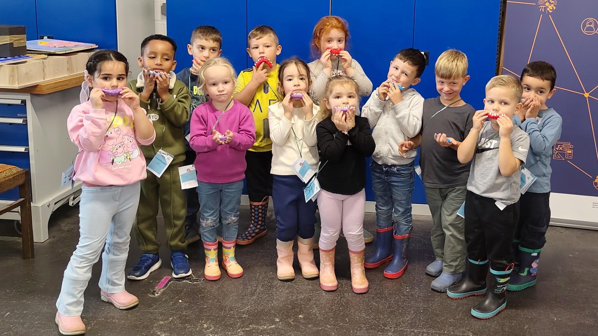 Es ist eine Gruppe von Kindergartenkindern zu sehen, wovon jedes ein selbst gebasteltes Gebiss hochhält.