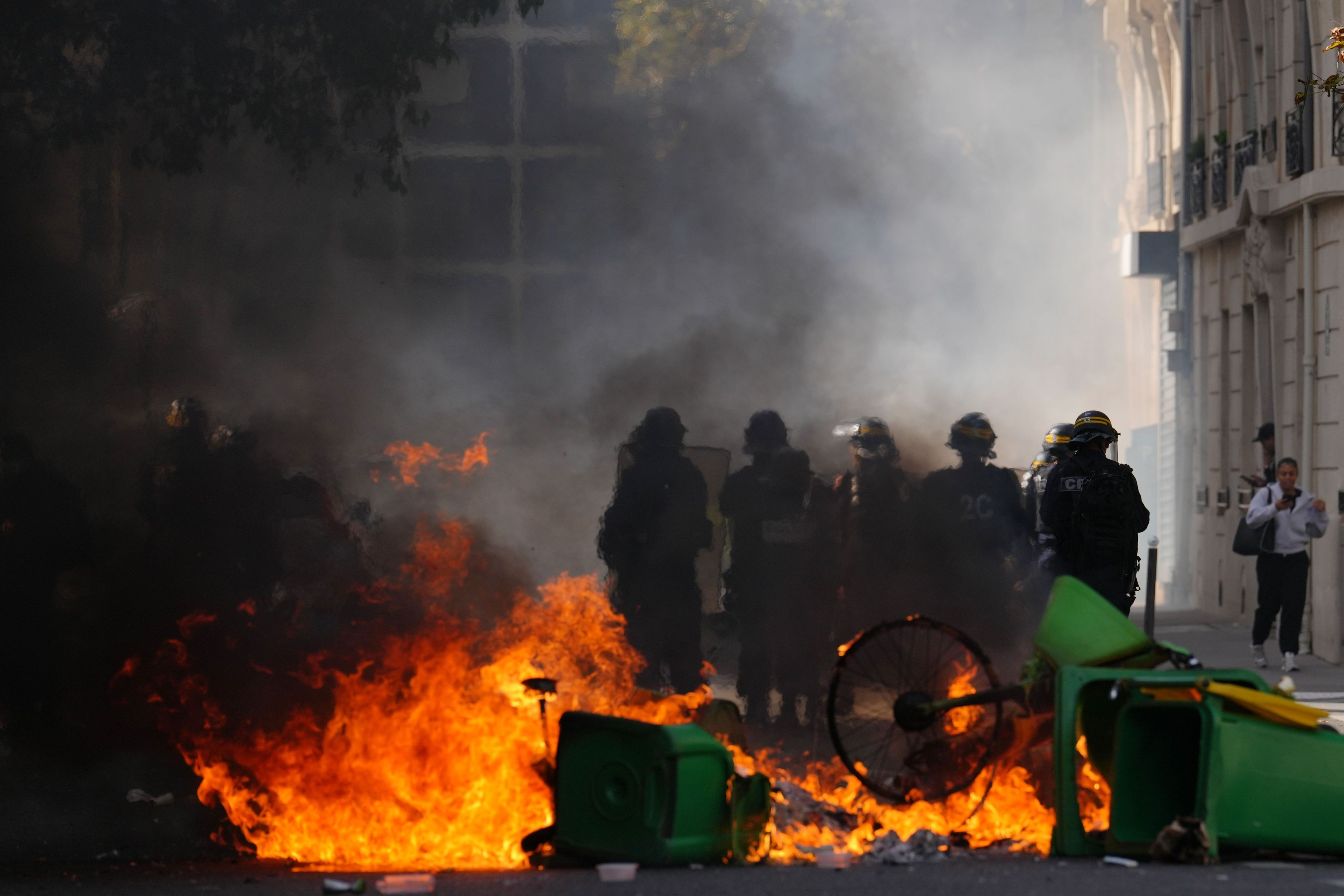 Polizisten stehen vor brennendem Müll, während sie bei einer Demonstration gegen unterfinanzierte Schulen Schülerinnen und Schülern gegenüberstehen.