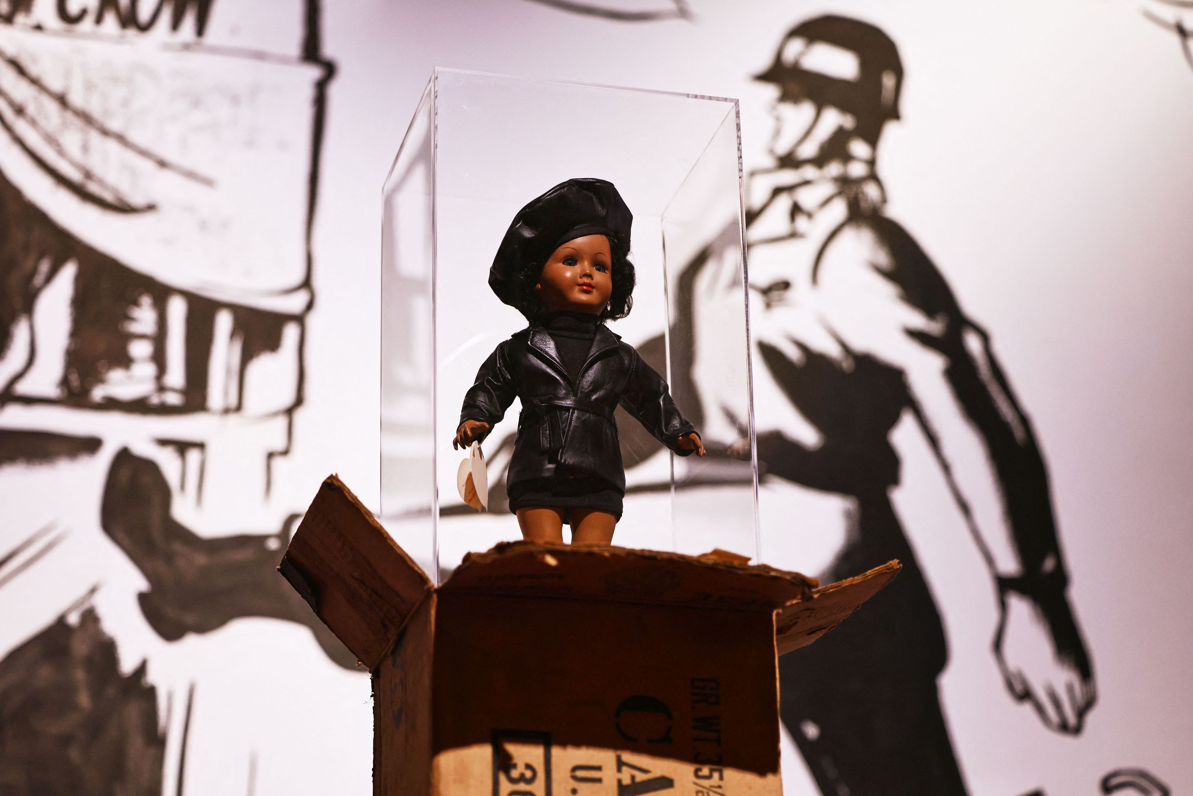 Die Puppe „Toxi“ von James Gregory Atkinson steht auf einem Care Paket in der Ausstellung «Along the Color Line - Spuren einer transatlantischen Moderne». Die Ausstellung ist vom 03.10.2026 bis zum 07.03.2027 im Museum Ludwig zu sehen.