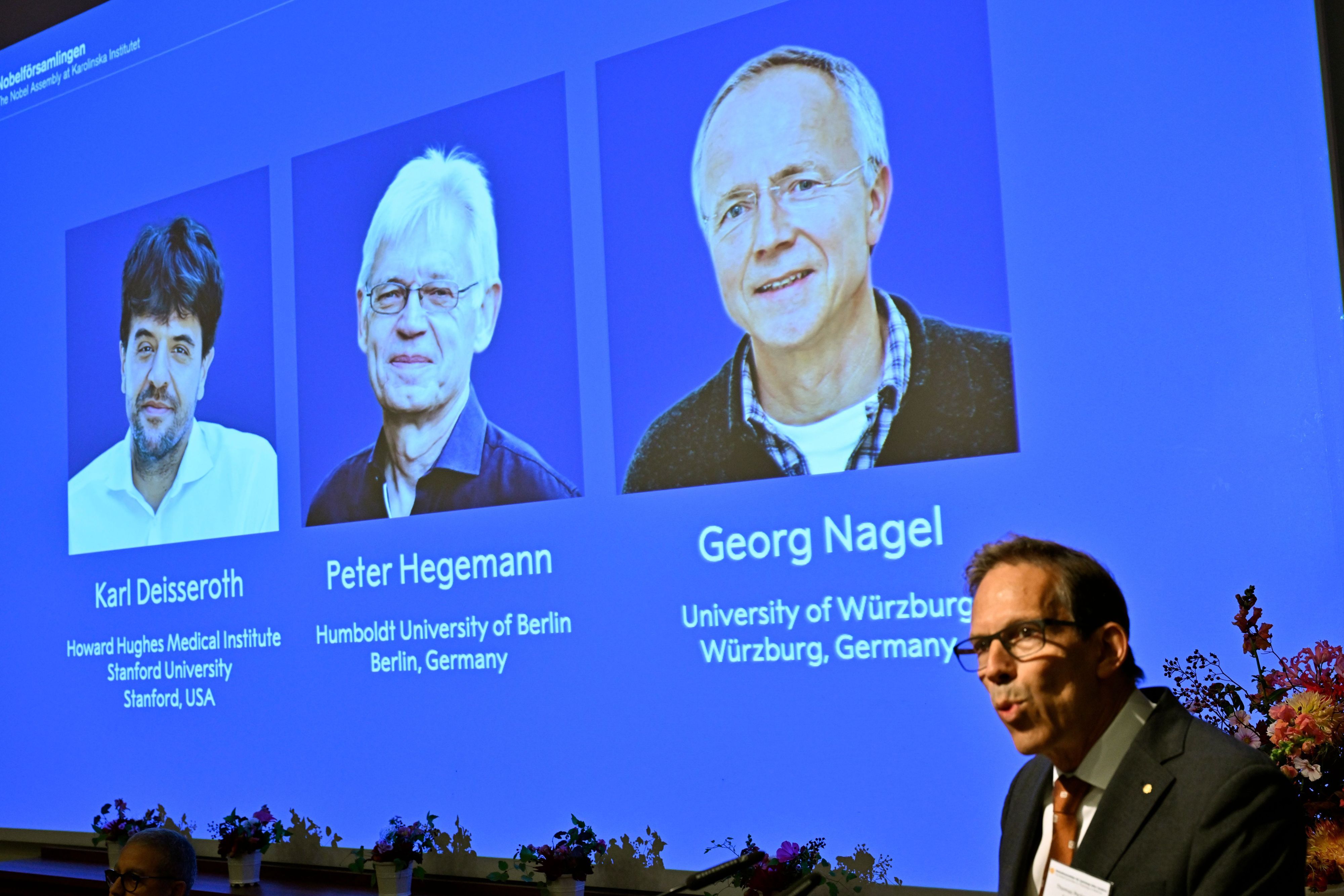 Karl Deisseroth, Peter Hegemann und Georg Nagel sind auf dem Bildschirm zu sehen, als ihnen der Nobelpreis für Physiologie oder Medizin 2026 verliehen wird.