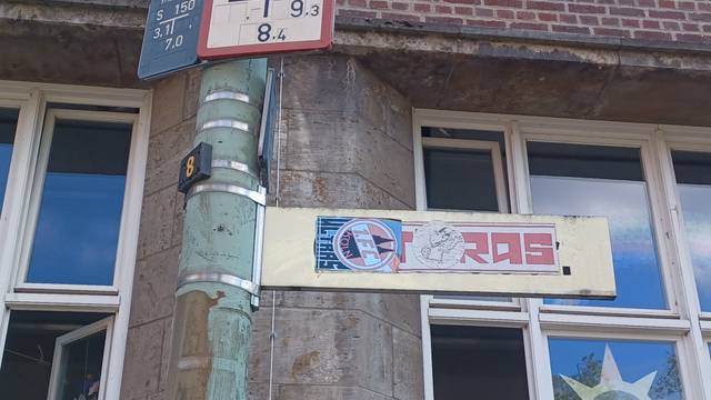 Ein mit FC‑Ultra-Aufklebern verunstaltetes Straßenschild steht vor einem Schulgebäude.