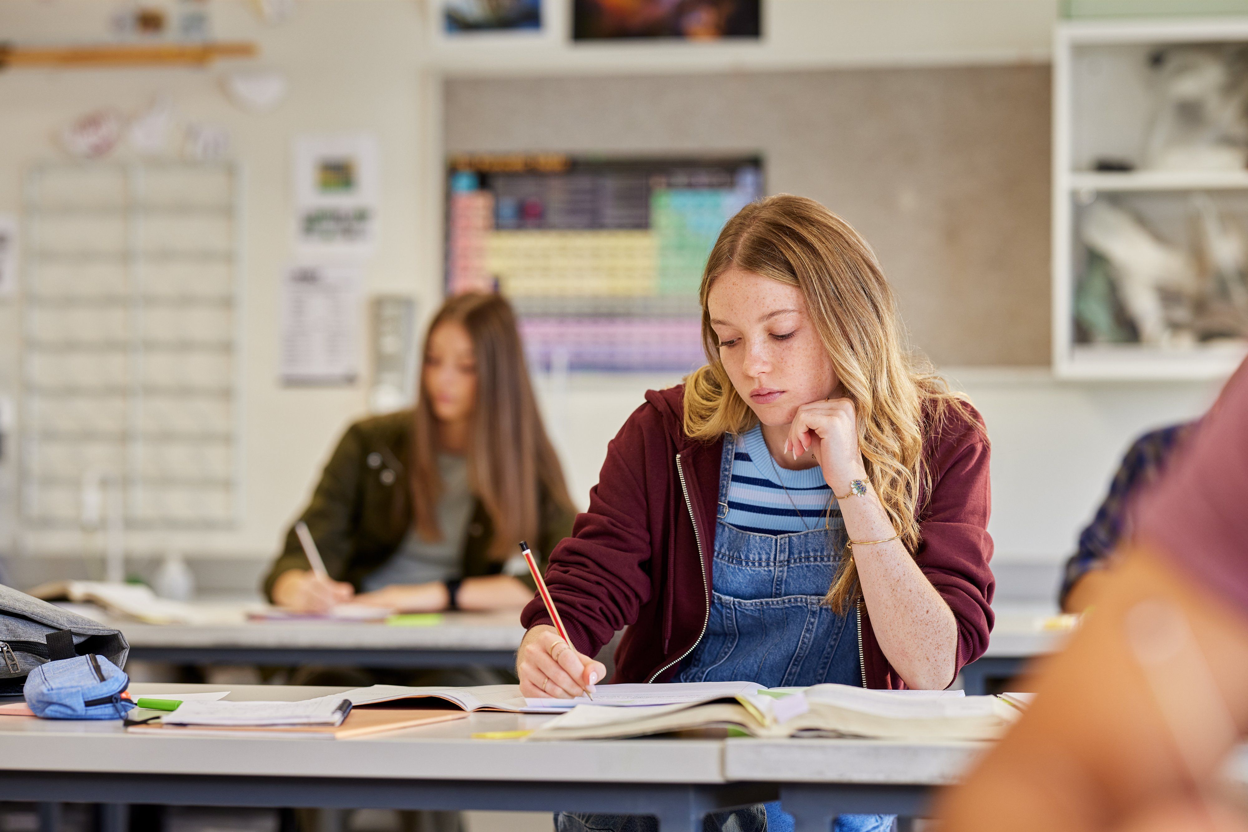 Schülerin schreibt konzentriert an ihren Aufgaben in einem hellen Klassenzimmer.