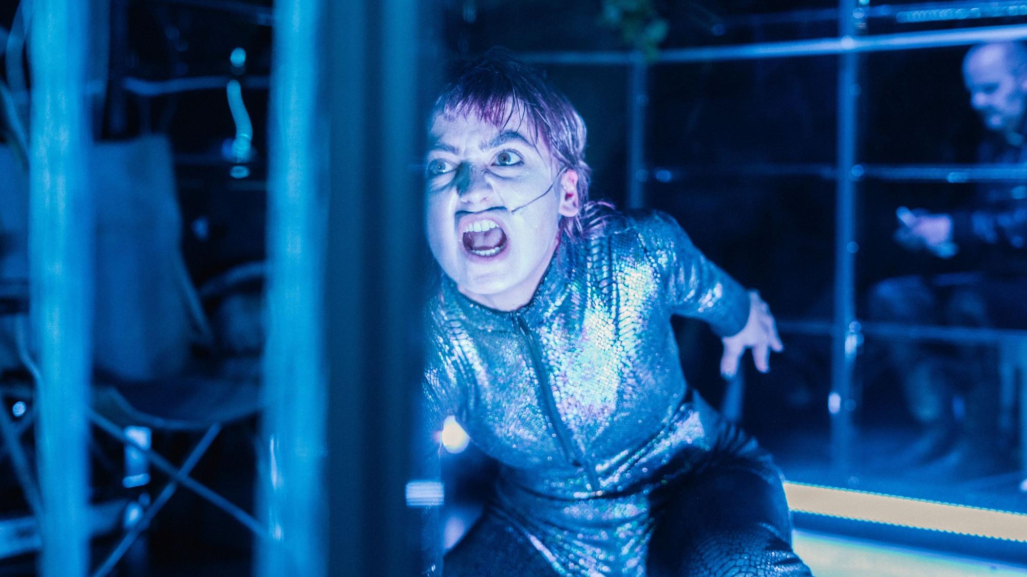 Eine Frau in einem glitzerfarbenen Neopren-Anzug schreit.