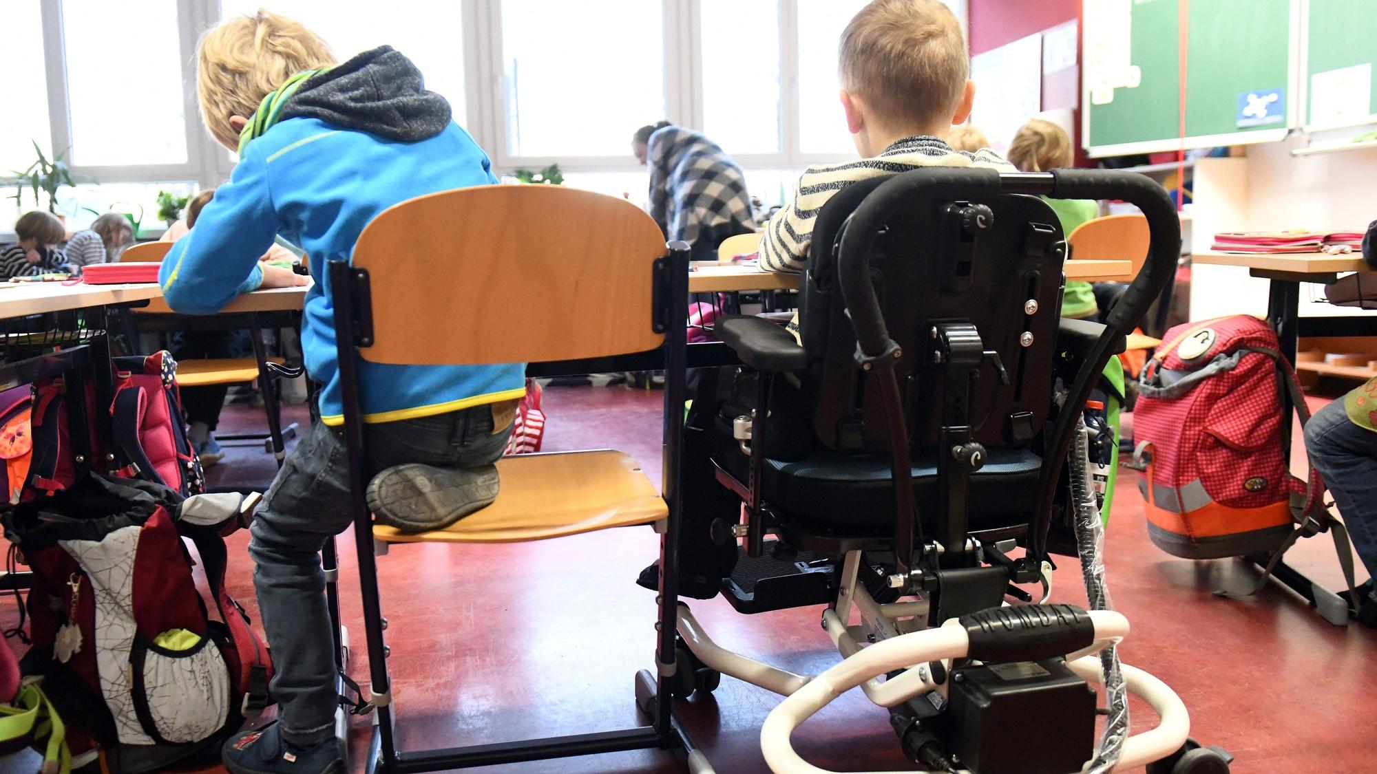 Ein Kind mit Behinderung sitzt in seinem Rollstuhl gemeinsam mit anderen Erstklässlern ohne Handicap in einem Klassenraum.