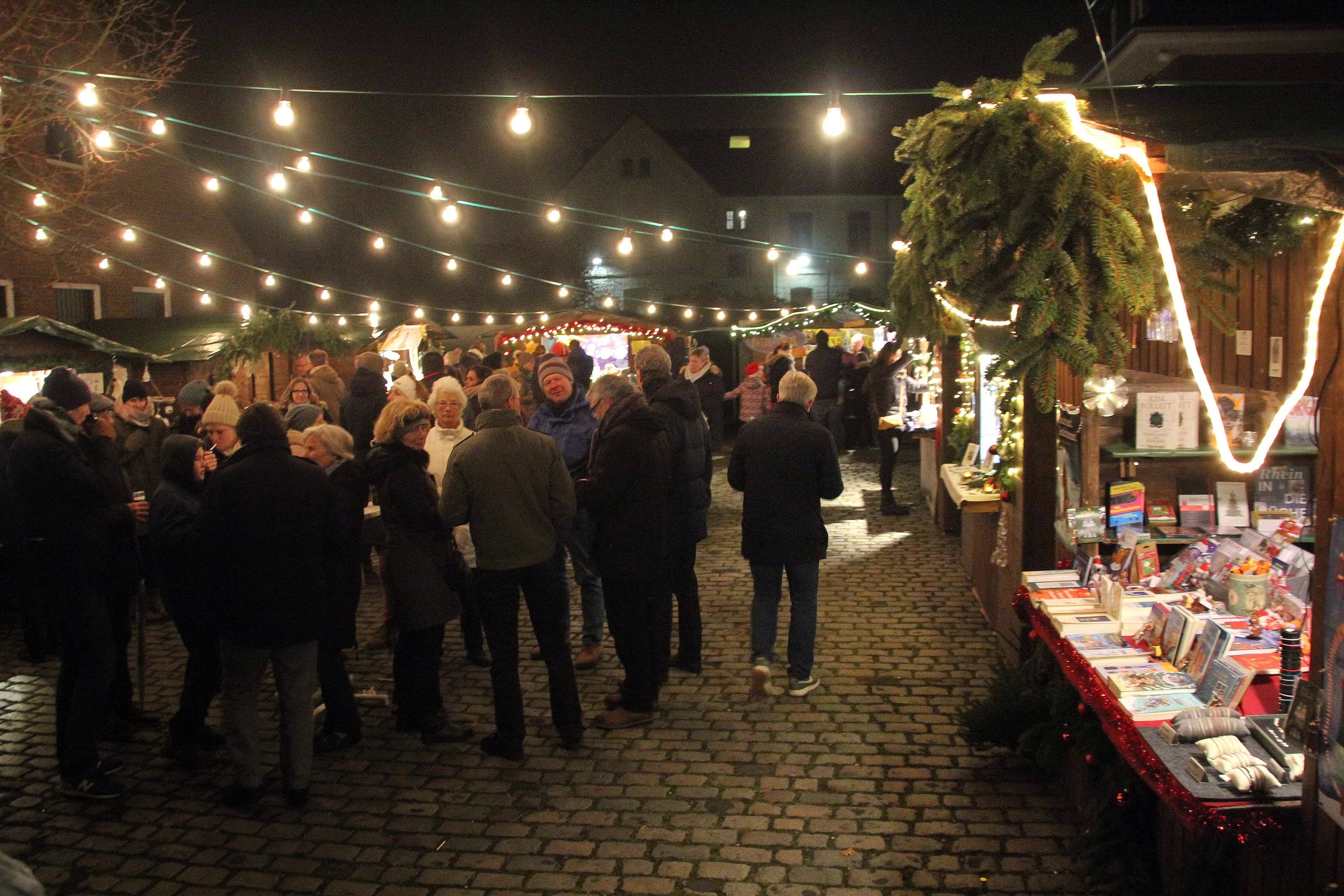 Auf einem Platz ist ein Weihnachtsmarkt mit Buden, Lichterketten und Weihnachtsbaum aufgebaut.