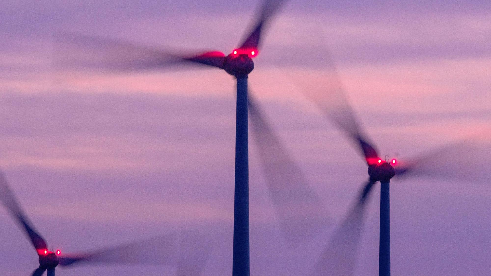 Mit Signallampen beleuchtete Windräder drehen sich nach Sonnenuntergang in einem Windpark.
