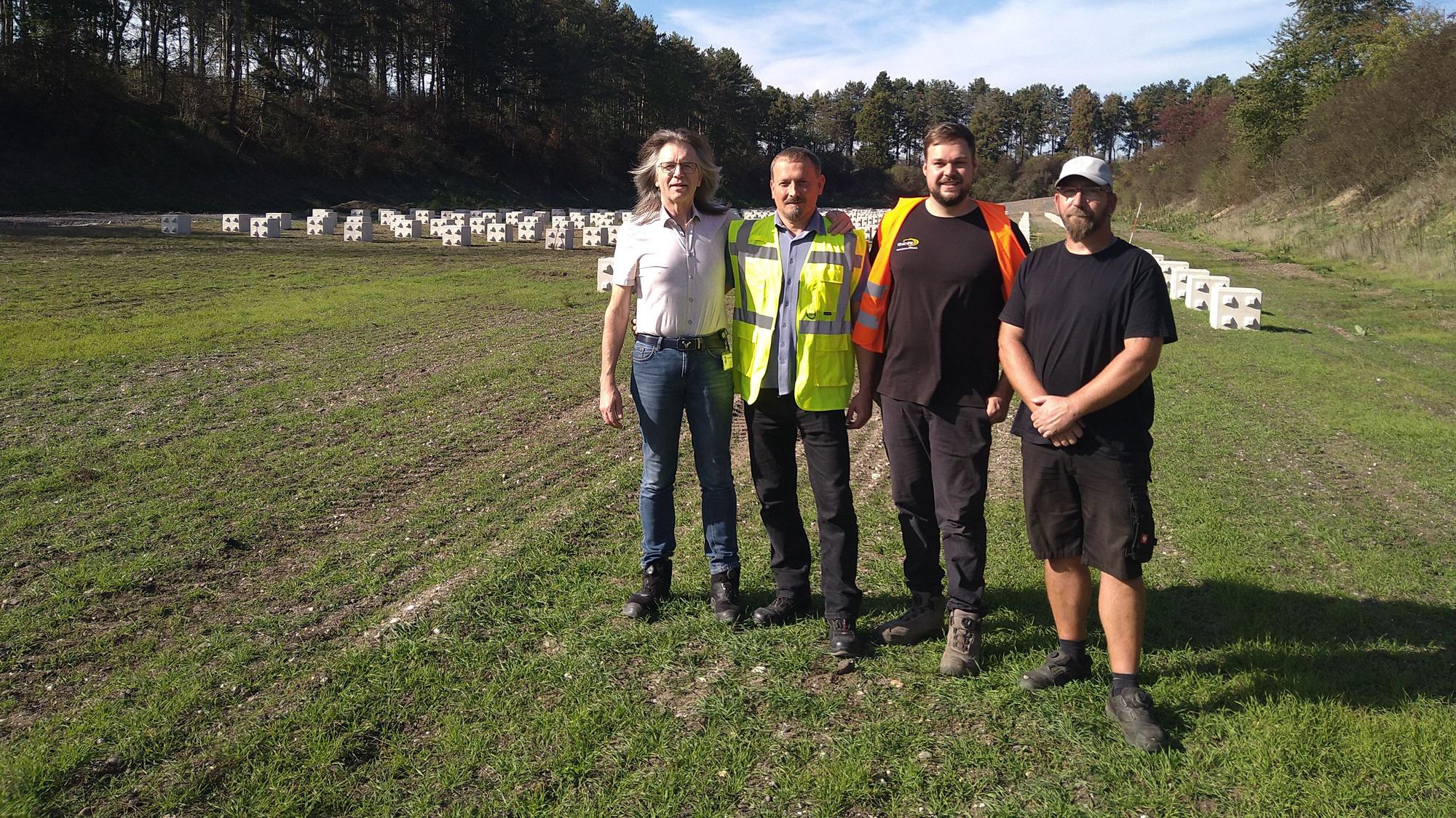 Vier Männer stehen auf einer großen Wiese, im Hintergrund sind PV-Elemente im Boden verankert.