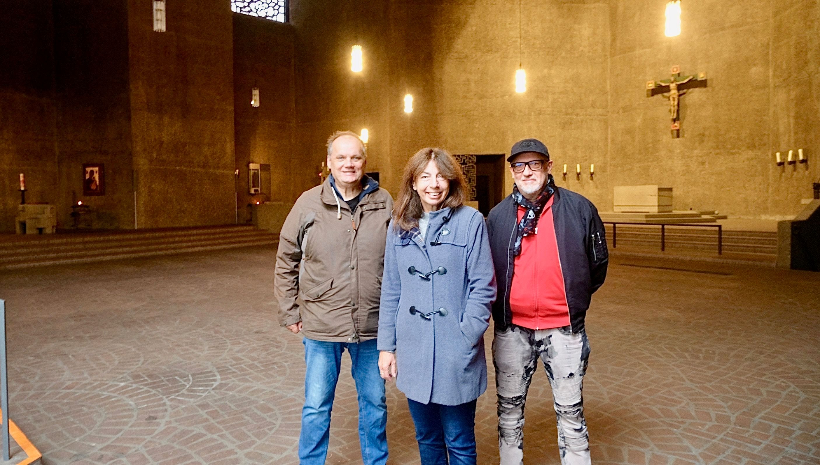 Zwei Männer und eine Frau stehen in einem leeren Kirchenraum.