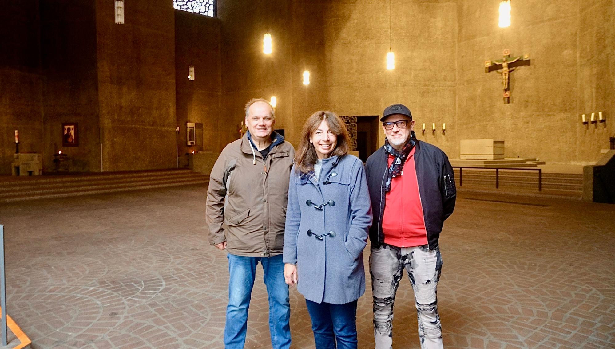 Zwei Männer und eine Frau stehen in einem leeren Kirchenraum.