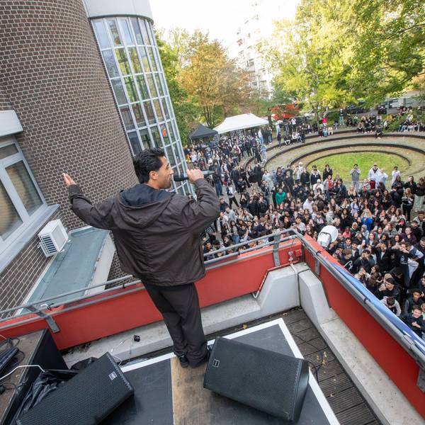 Ein junger Mann singt auf einer Dachterrasse. Unten auf dem Rasen steht eine jubelnde Menge.