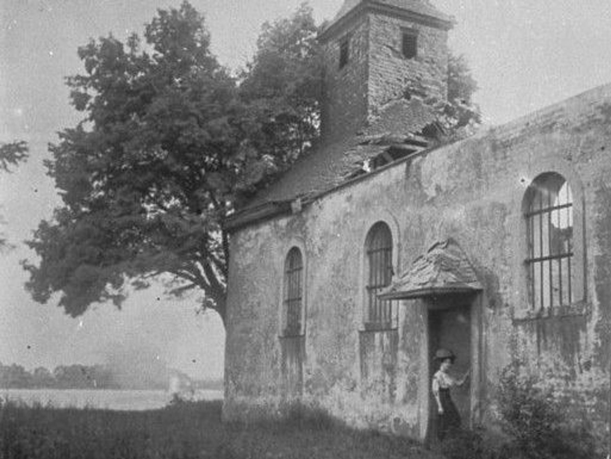 Ein Schwarz-Weiß-Foto zeigt eine kleine Kirche, dahinter ist der Rhein zu sehen.