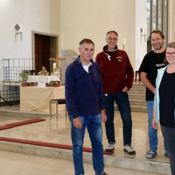 Drei Männer und eine Frau stehen im Altarraum einer Kirche, wo verschiedene Krippenfiguren aufgebaut sind.