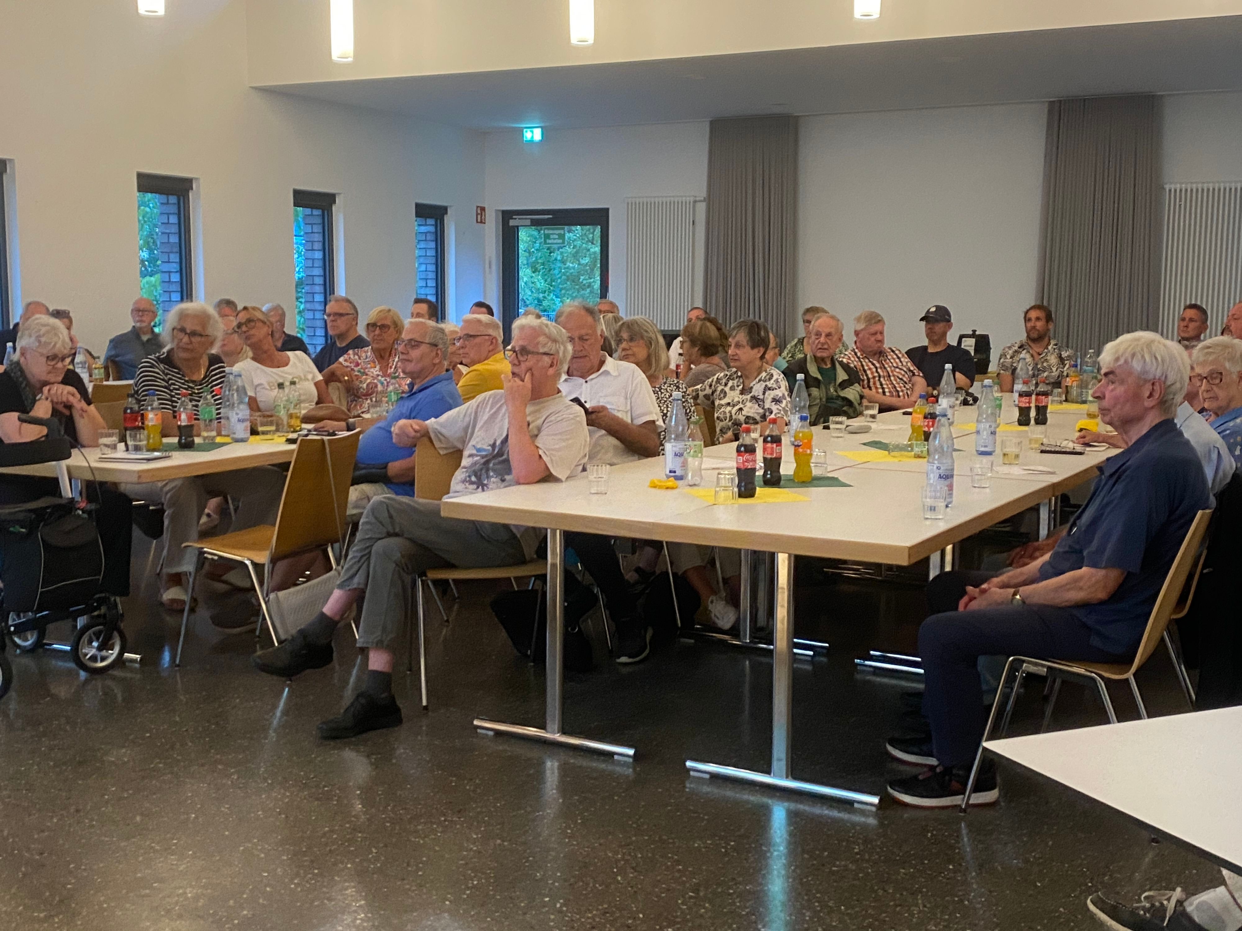 An großen Tischen sitzen überwiegend ältere Menschen.