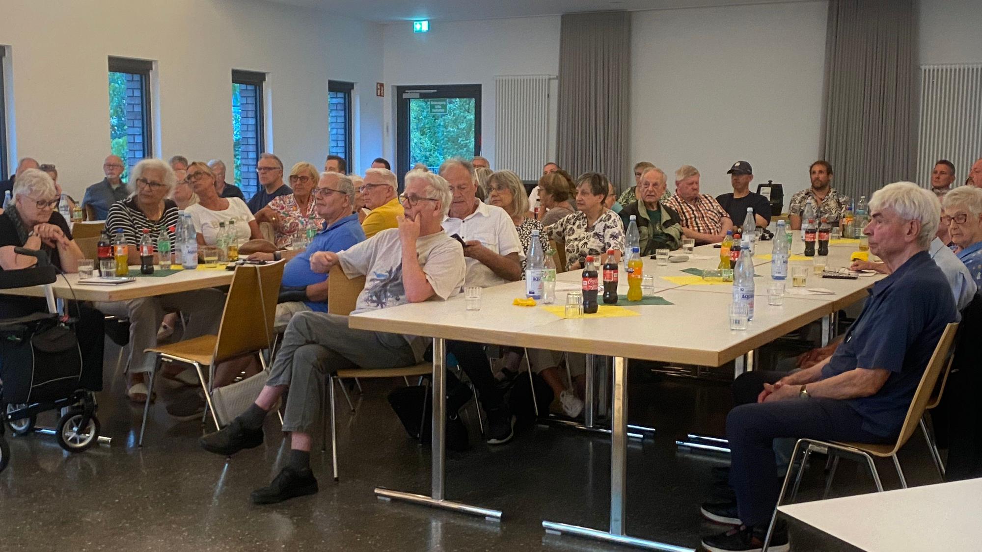 An großen Tischen sitzen überwiegend ältere Menschen.
