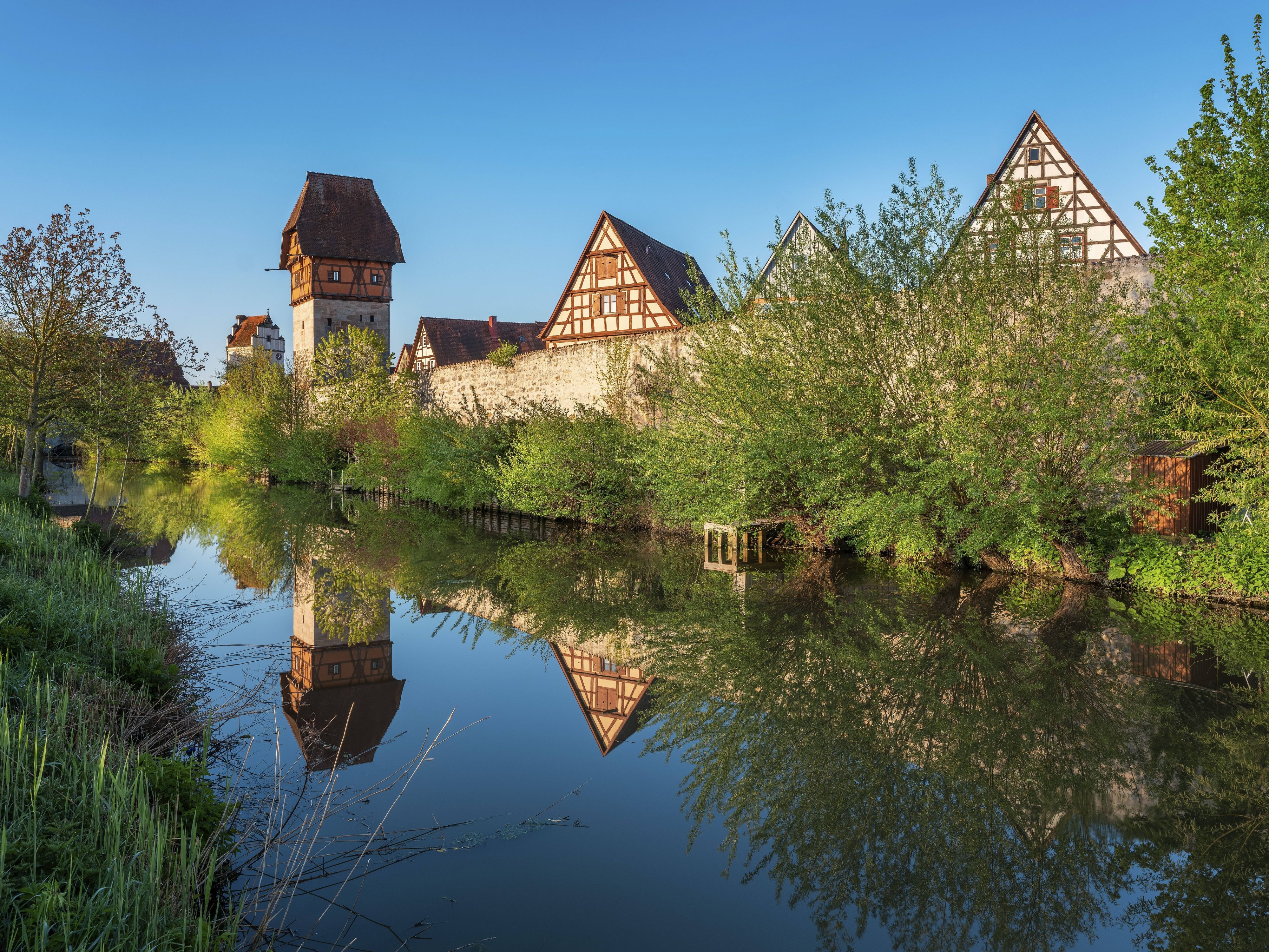Die historische Stadtmauer von Dinkelsbühl an der Romantischen Straße spiegelt sich samt ihren Wehrgängen, Wehrtürmen und alten Fachwerkhäusern im Wasser des Mühlgrabens der Wörnitz.