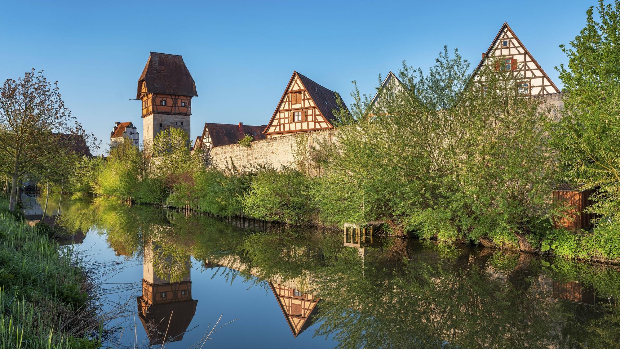 Die historische Stadtmauer von Dinkelsbühl an der Romantischen Straße spiegelt sich samt ihren Wehrgängen, Wehrtürmen und alten Fachwerkhäusern im Wasser des Mühlgrabens der Wörnitz.