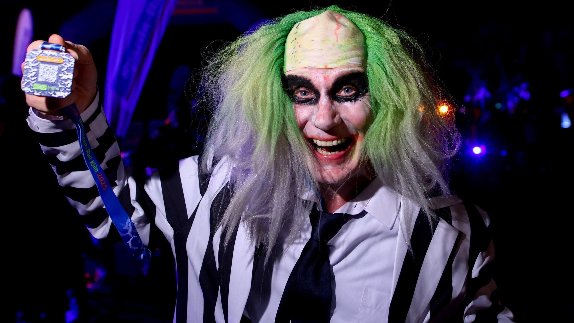 Kostümierte Läufer starten beim Halloween-Run durch den Botanischen Garten bei der im Dunklen auf einer beleuchteten Laufstrecke gelaufen wird - Norbert zeigt seine Medaille.