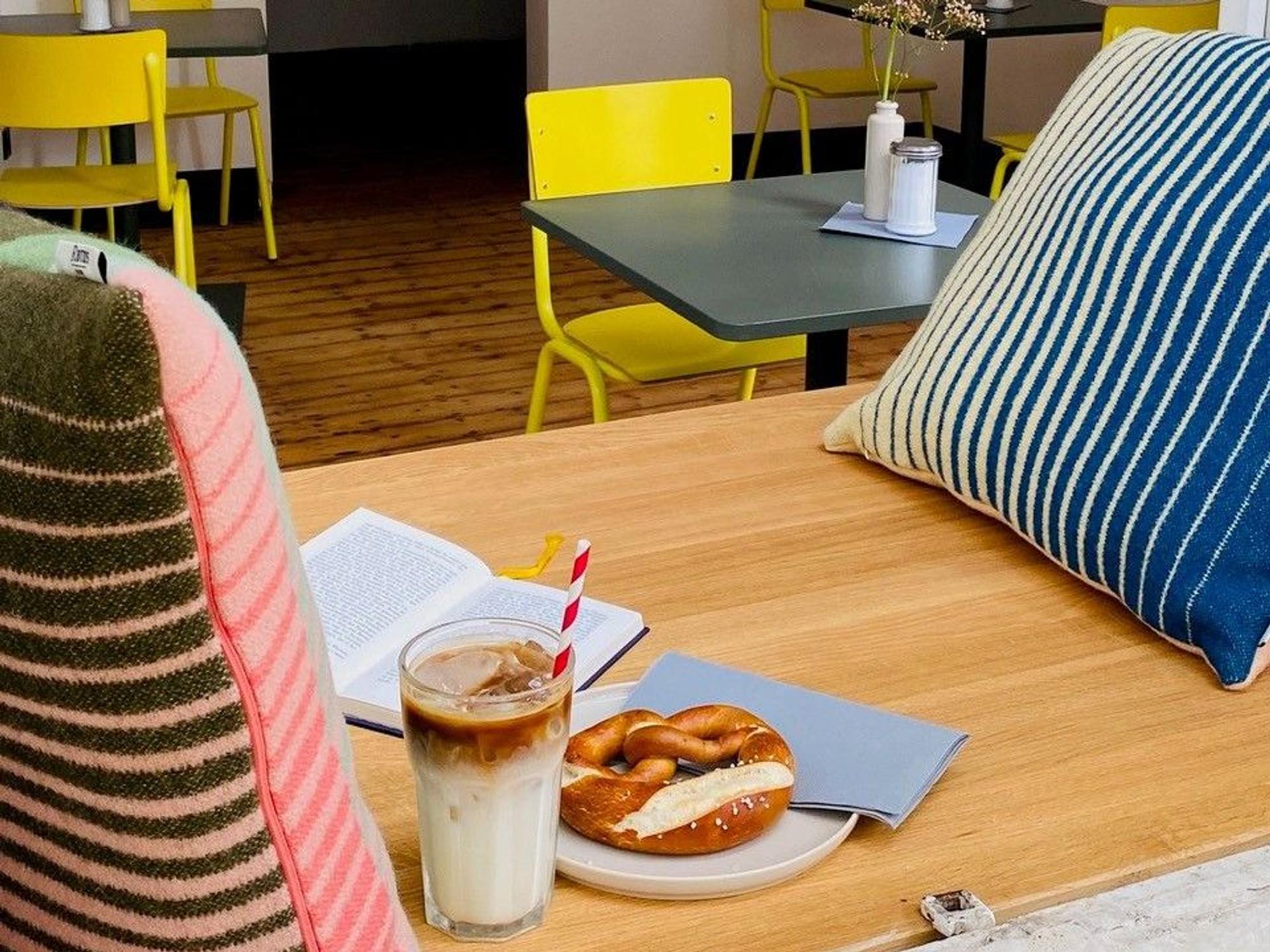 Brezel, Getränk und Altbau-Charme mit Holzdielen und gelben Stühlen bei „Die Brezel“.