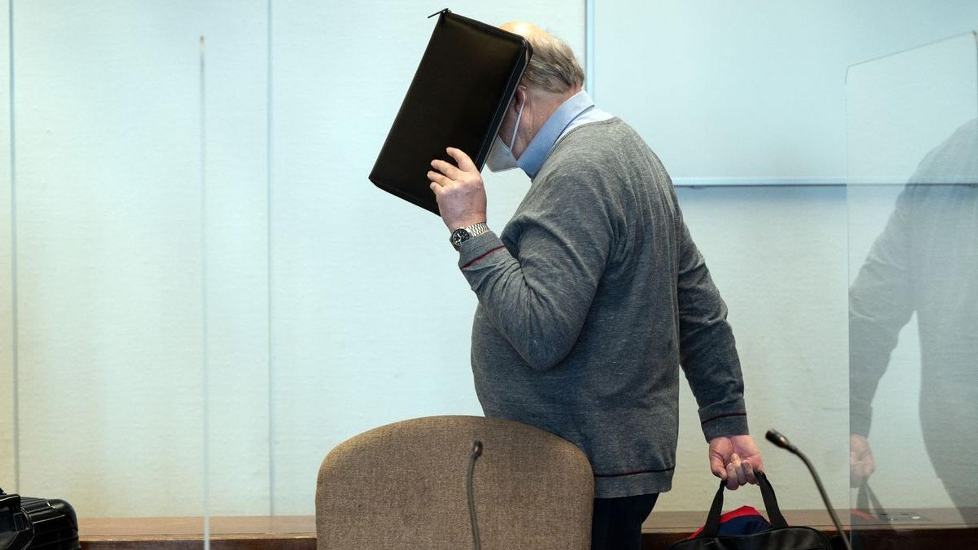 Der angeklagte katholische Priester hält sich im Gerichtssaal eine Mappe vor das Gesicht.