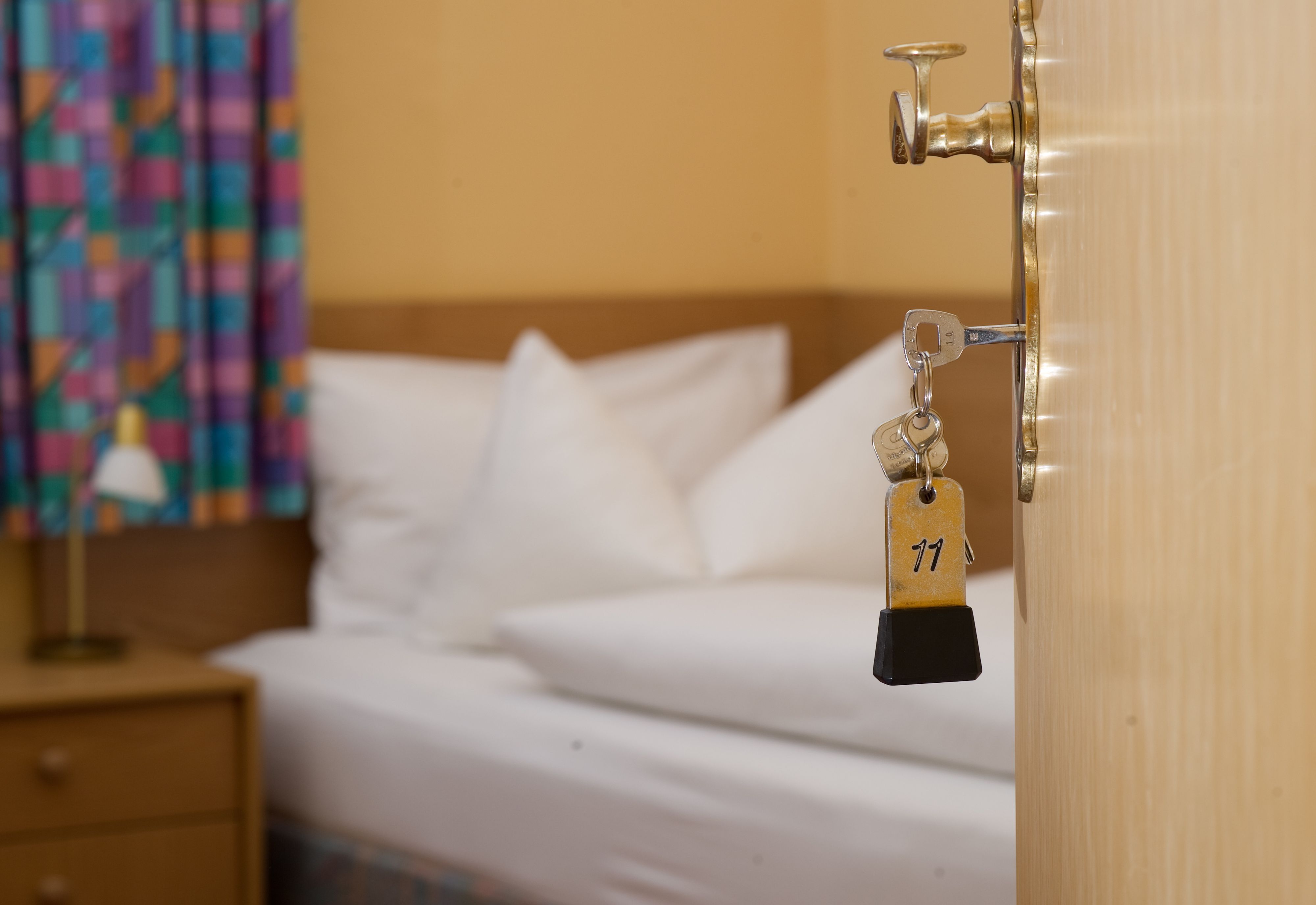 Ein Zimmerschlüssel hängt in einem Gästehaus vor einem Bett im Türschloss.
